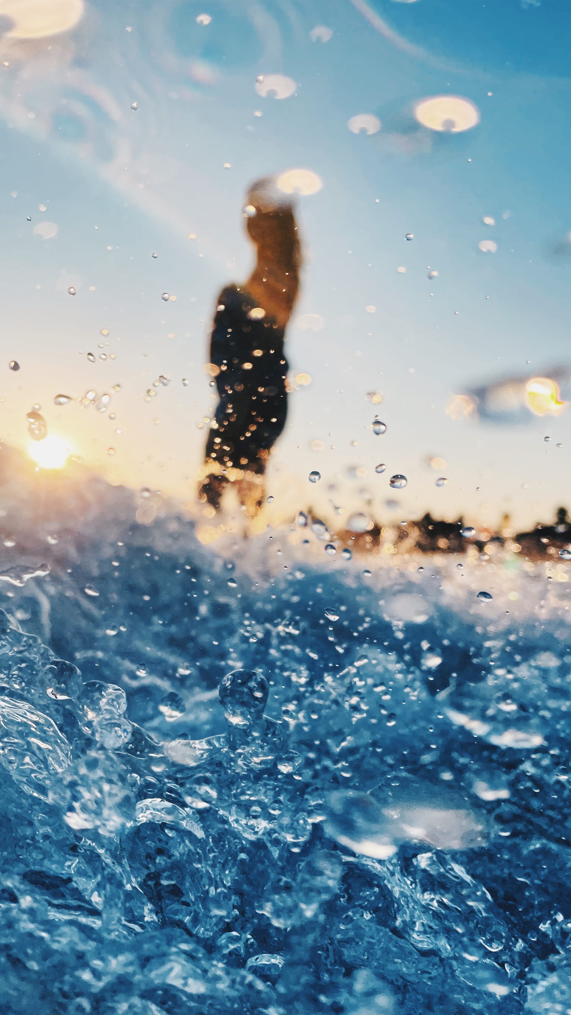 Bright blue splashing water and suspended droplets fill the foreground beneath a blurred standing figure.