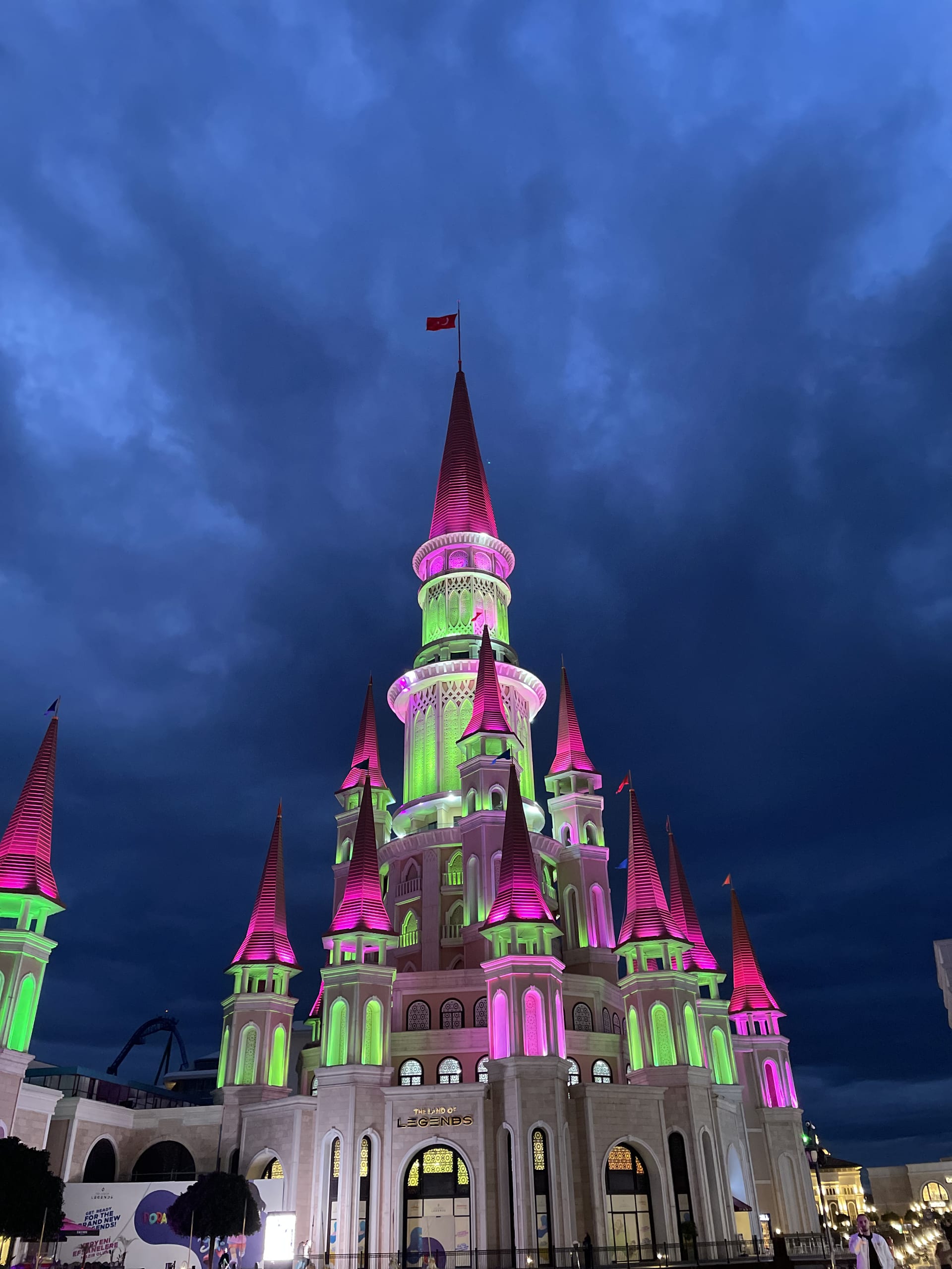 A castle-like building glows in vivid pink and green beneath a dark, cloud-filled sky.