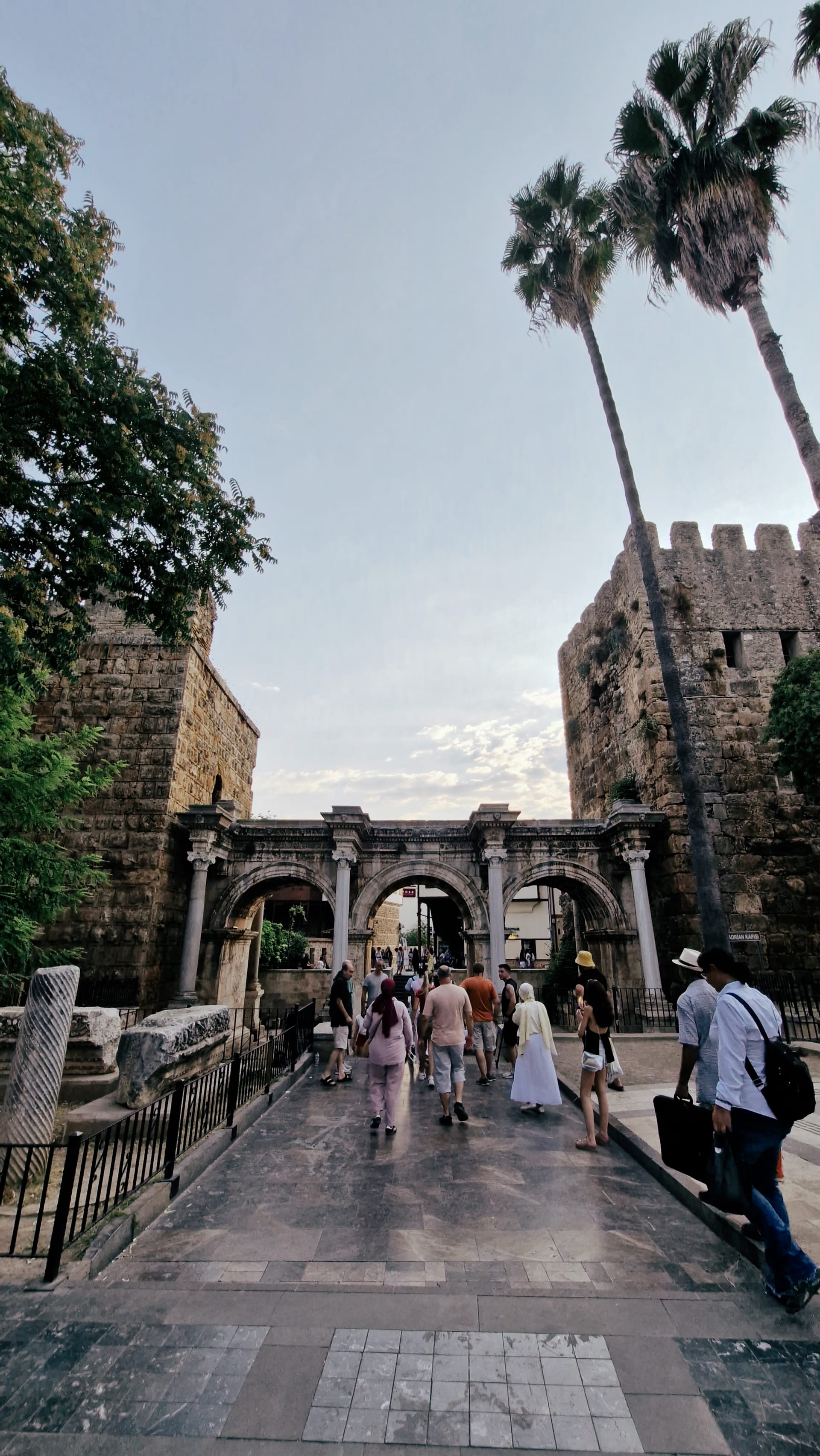 Three-arched stone gate between towers with visitors gathered beneath it.