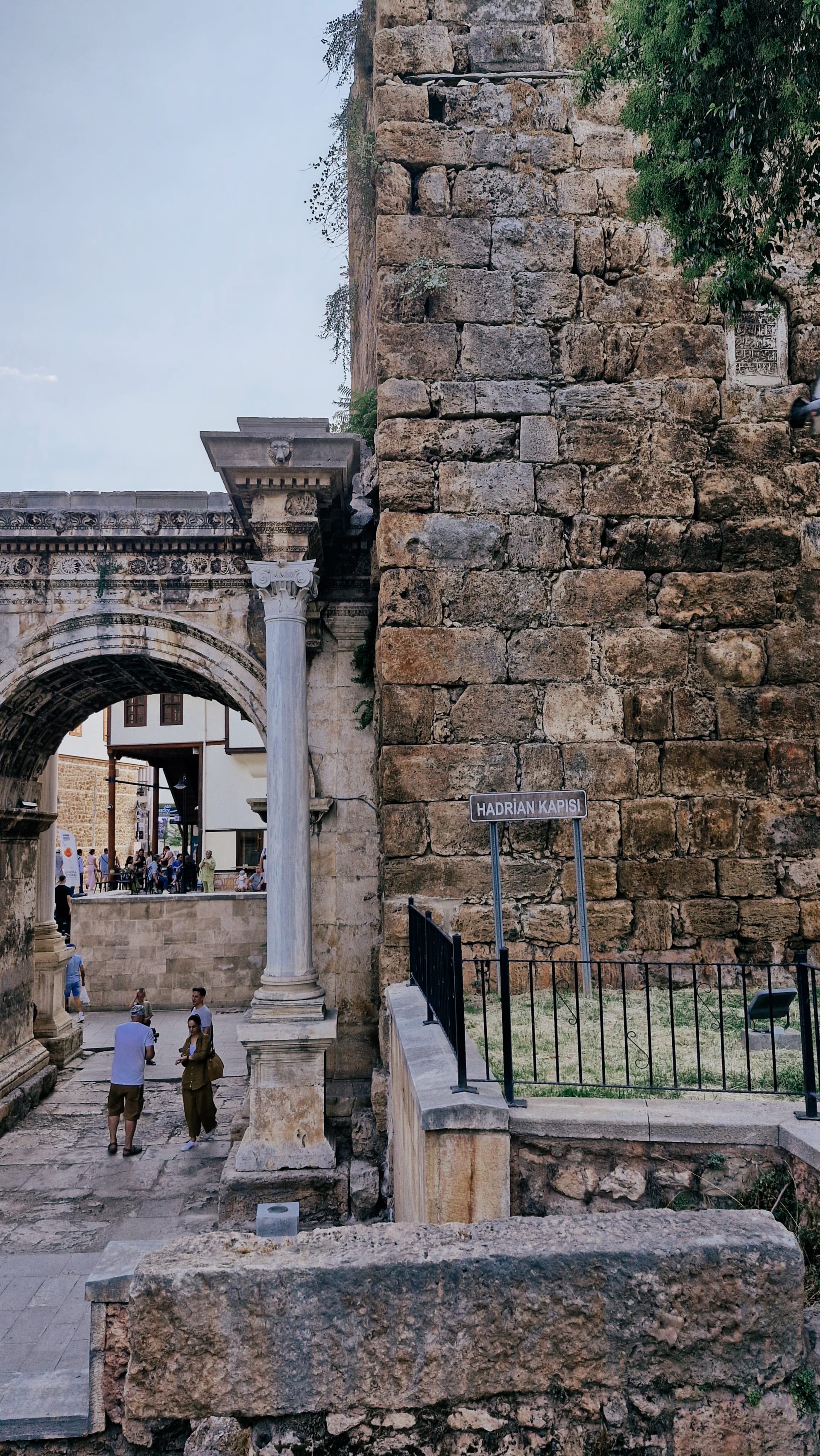 Side view of a stone tower, one gate arch and visitors behind railings.