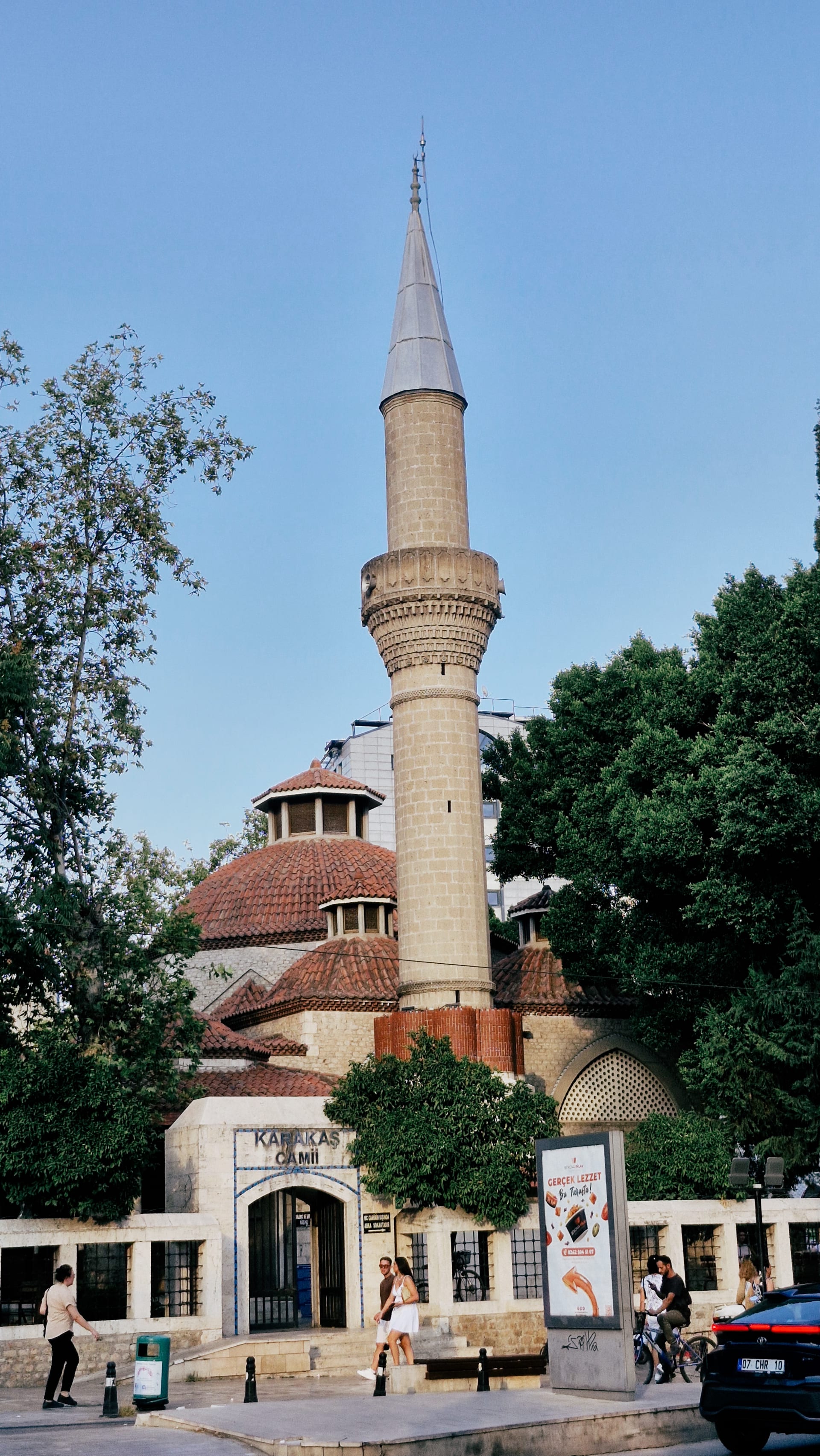 Slender mosque minaret and red-roofed dome seen beyond trees near the gate.