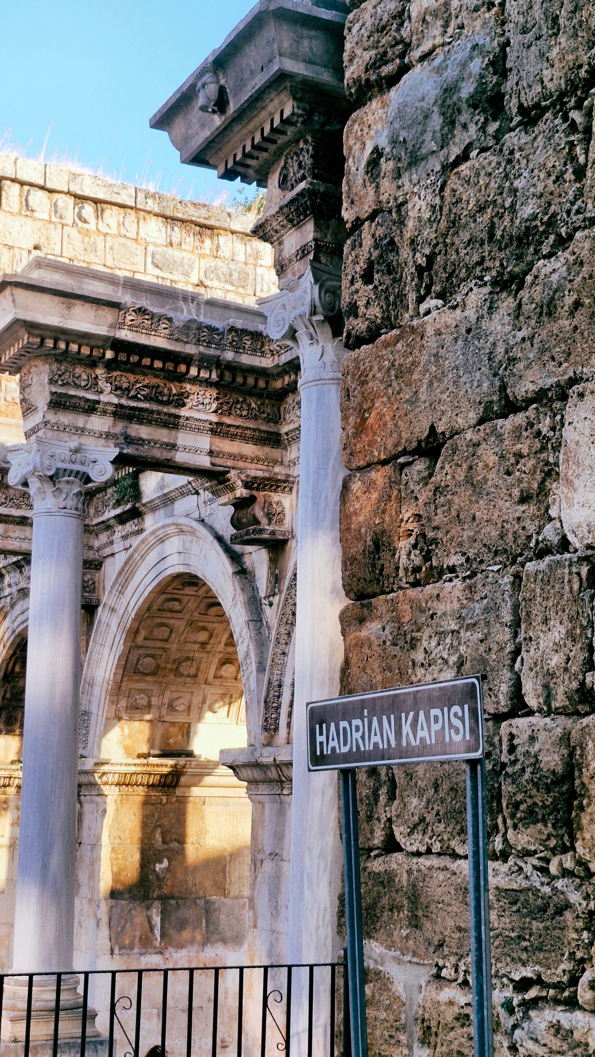 Blue Hadrian Kapısı sign beside a stone arch and tower wall.