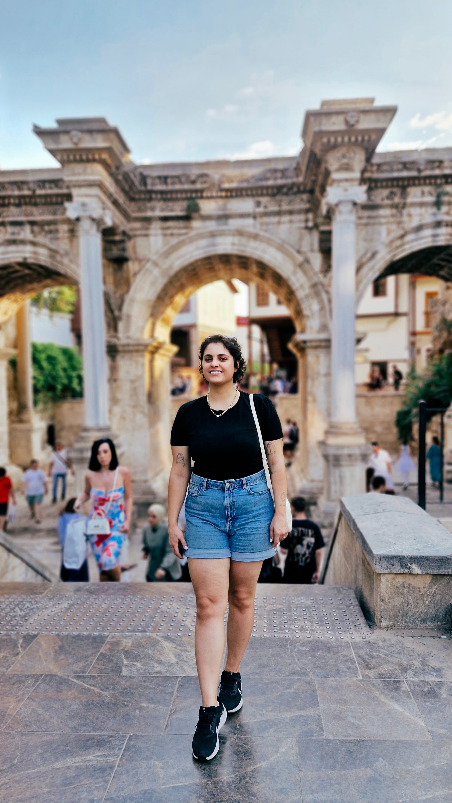 Woman walking towards the camera with the central arch and visitors behind her.