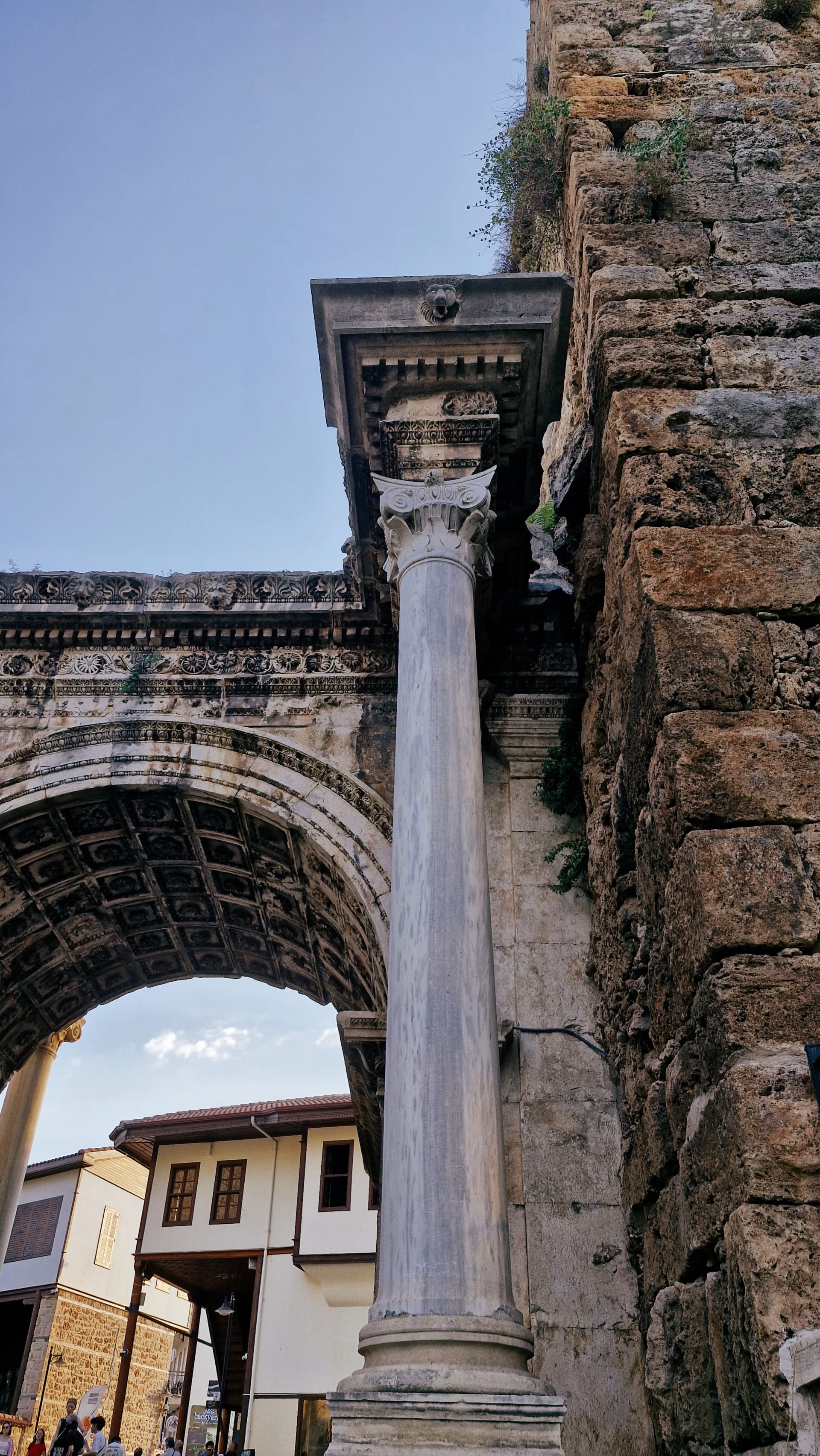 White column beside a coffered arch, rough tower and old-town houses.