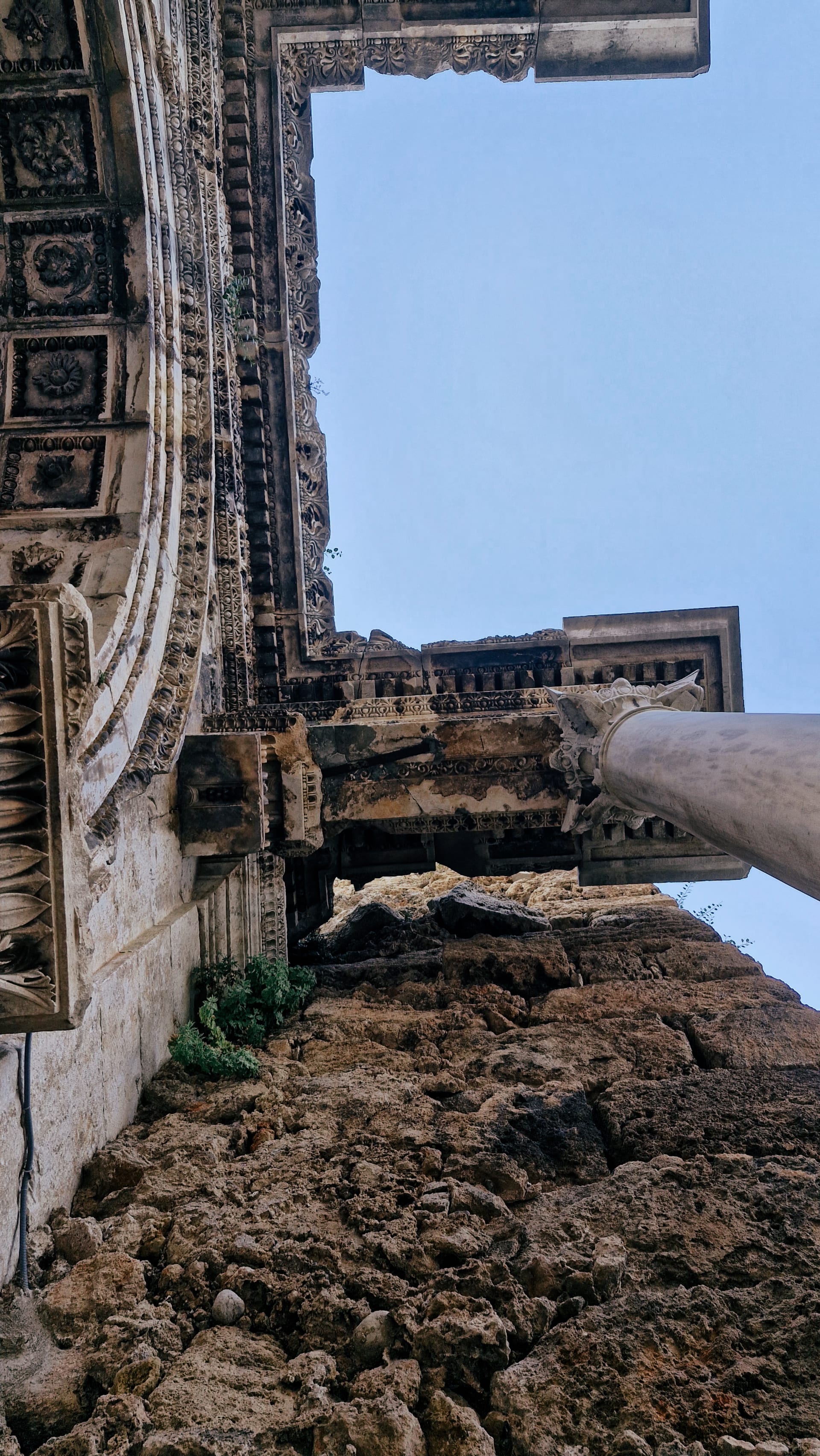 Steep upward view between a rough stone tower, arch and white column.