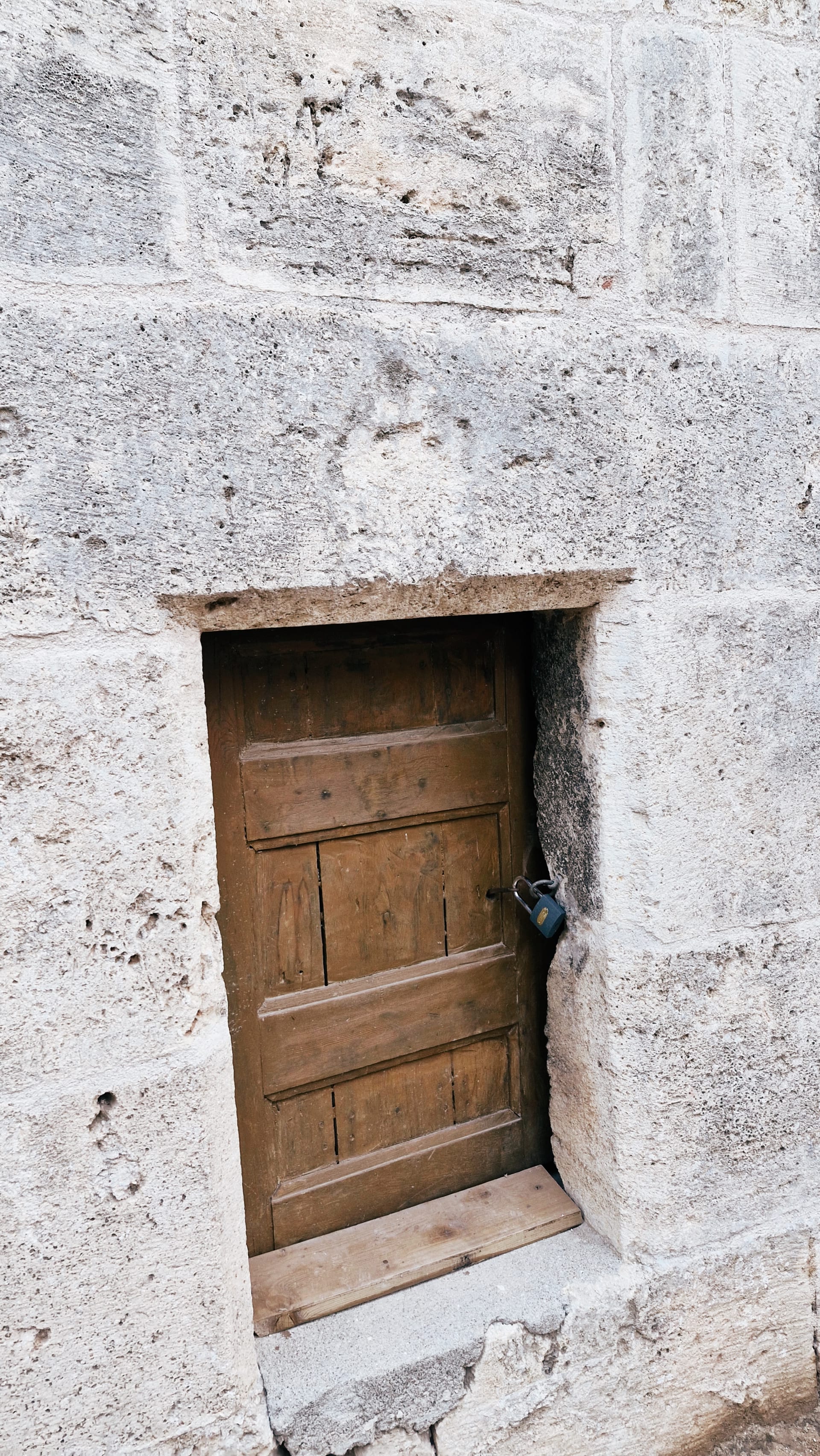 Small plain wooden door set into a pale stone wall.