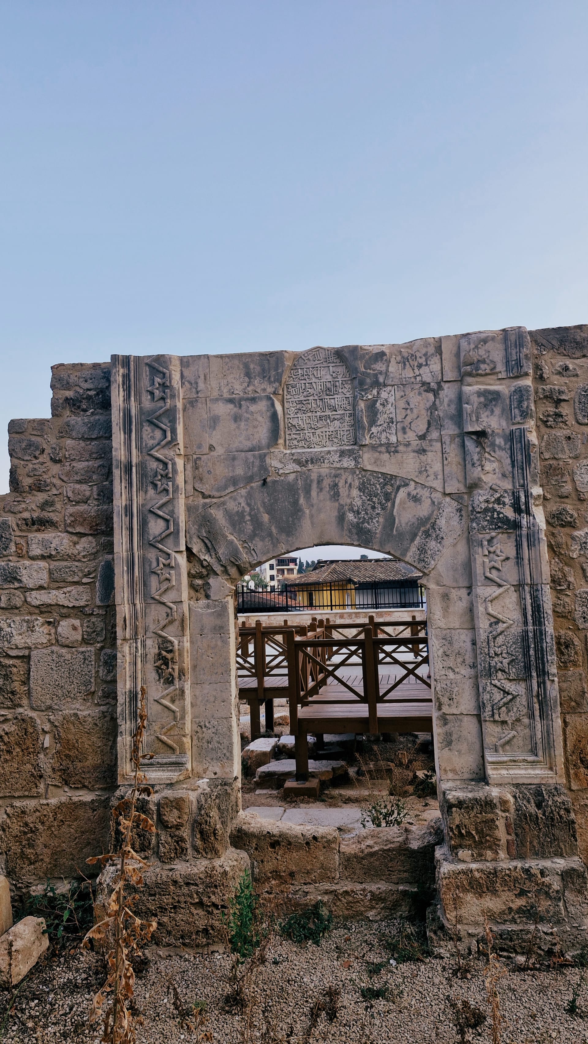 Weathered stone opening framed by carved vertical bands and low ruins.