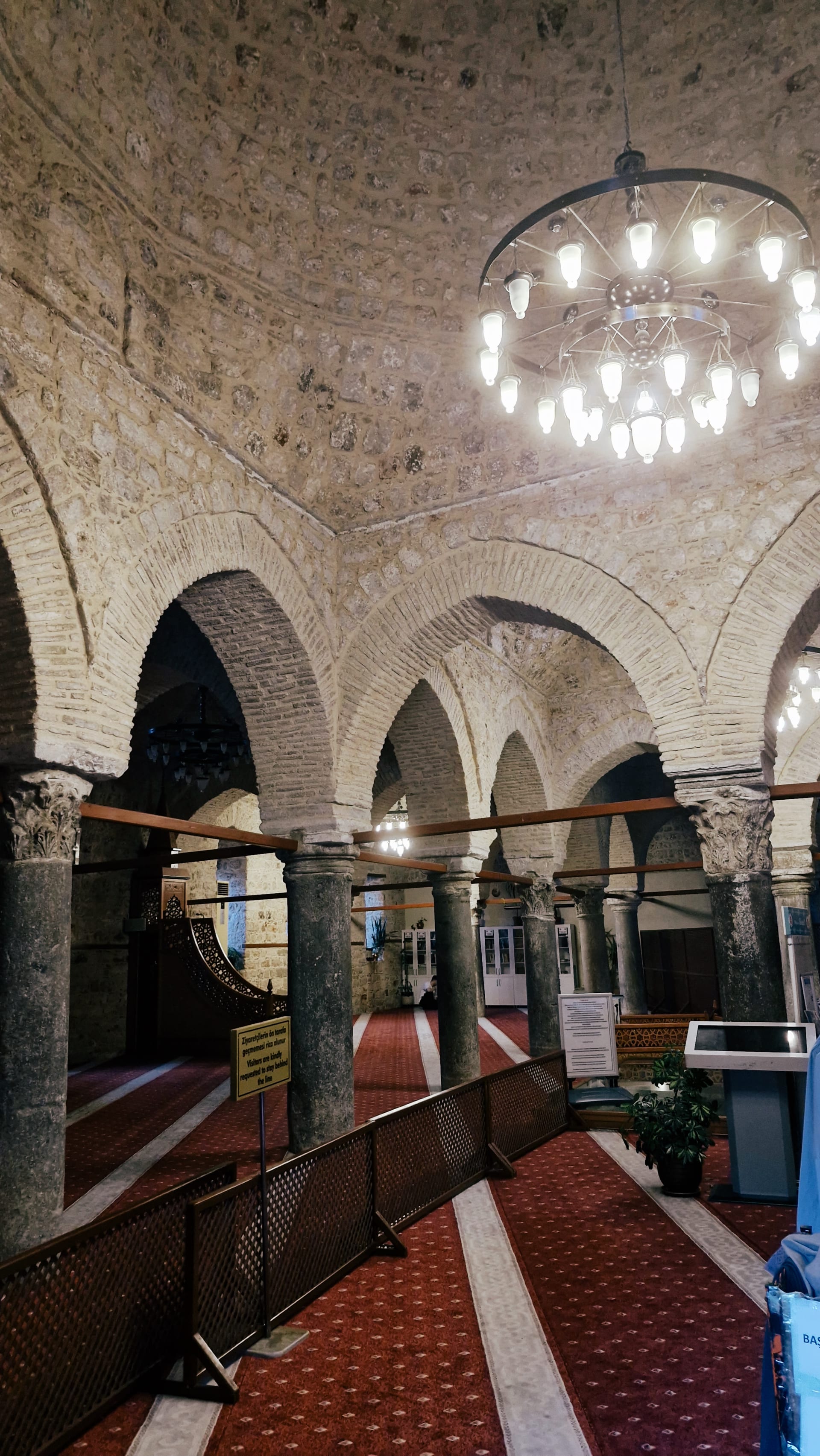 Broad mosque interior with pointed stone arches, red carpet and circular chandeliers.
