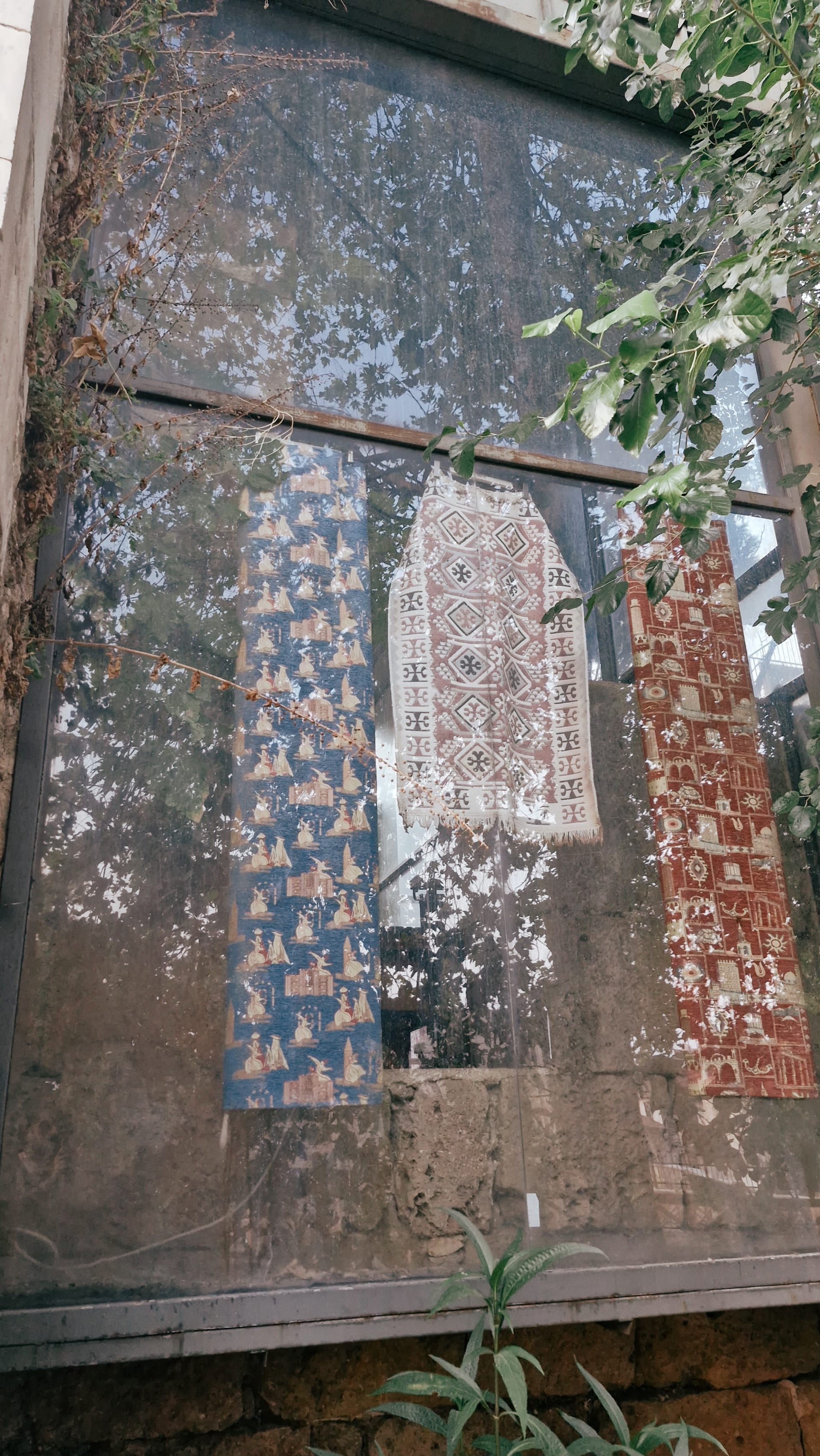 Colorful patterned textiles hanging behind reflective glass outdoors.