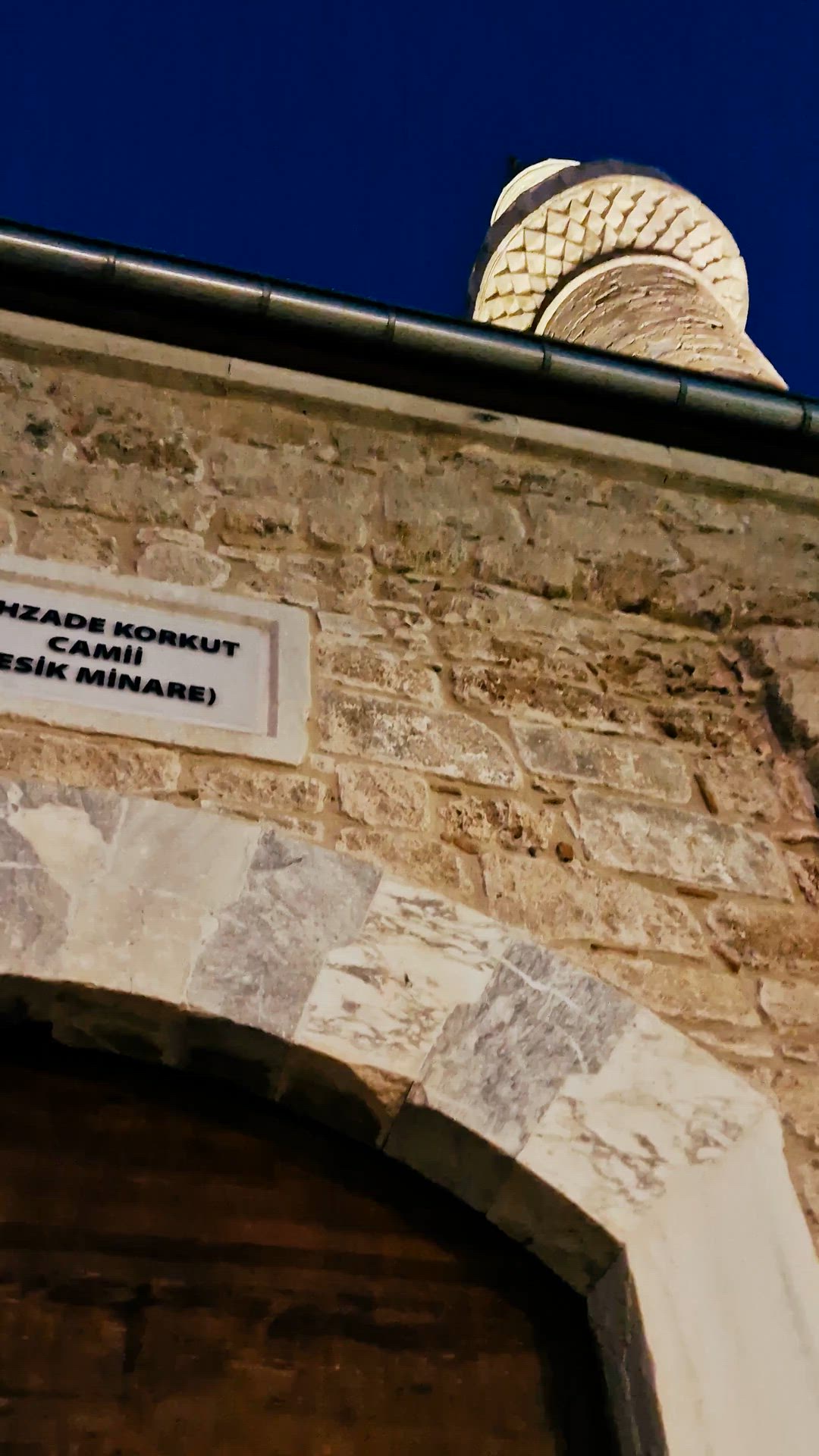 Video entering through a stone passage past hanging visitor garments toward the prayer hall.
