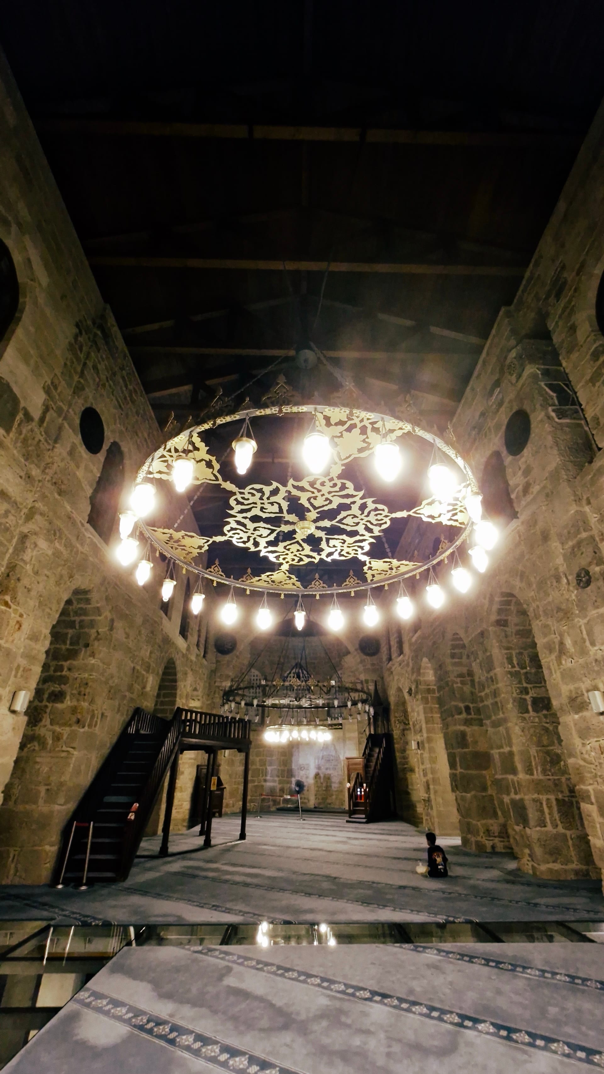Deep view through the prayer hall beneath a bright circular chandelier.