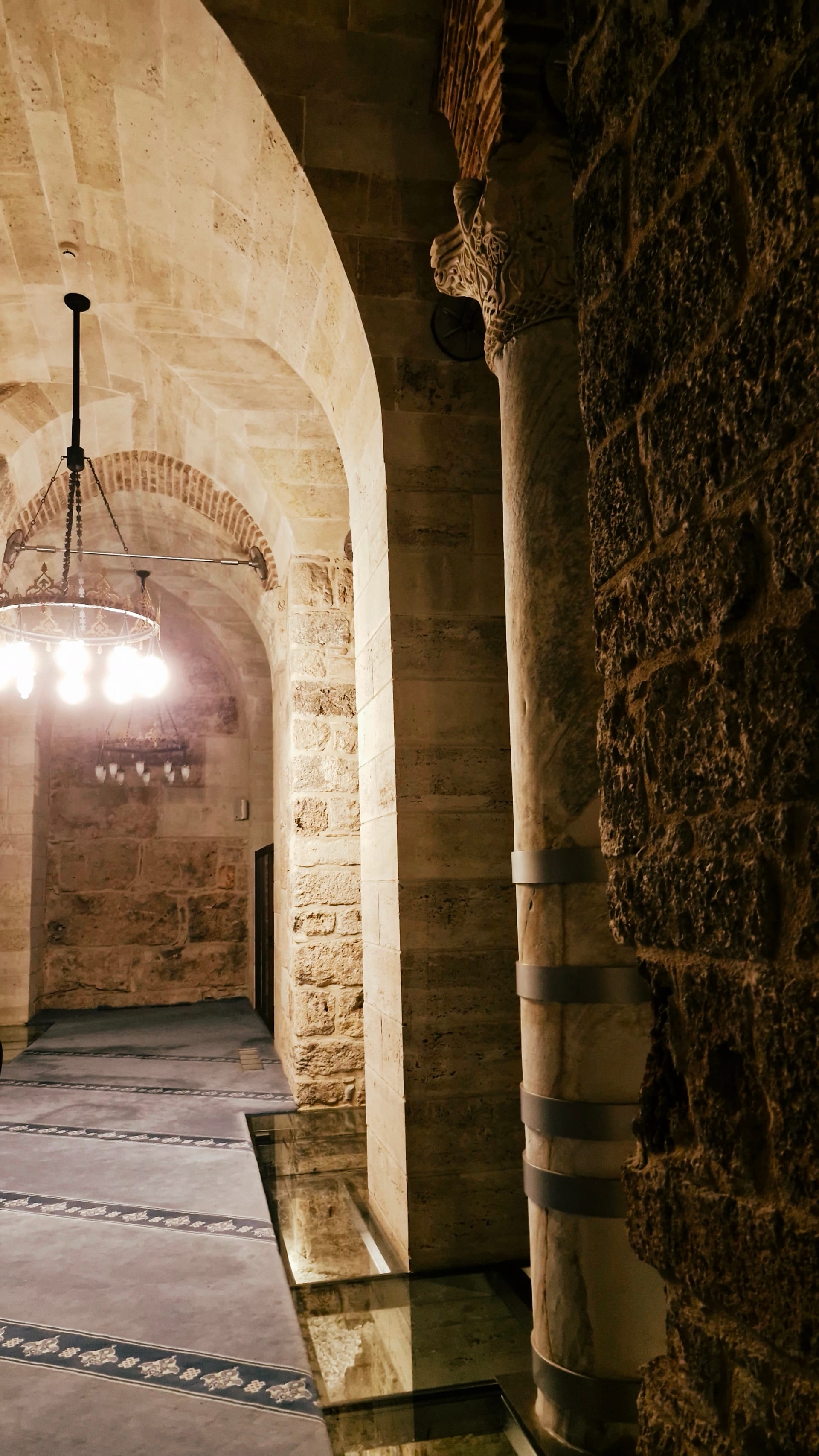 Layered stone arches and columns with a circular light beyond.