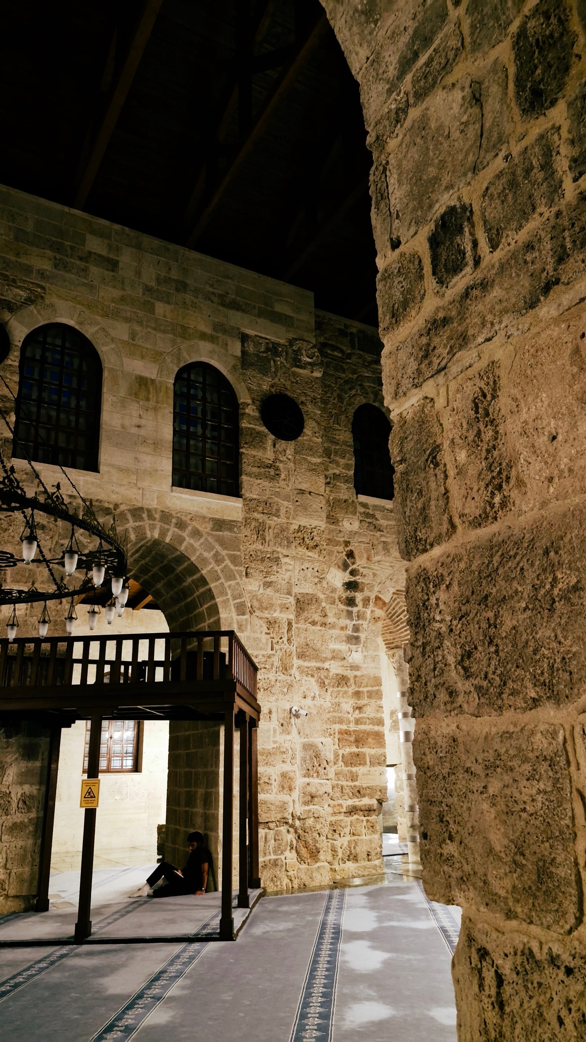 High interior walls with arched windows, a stone opening and timber gallery.