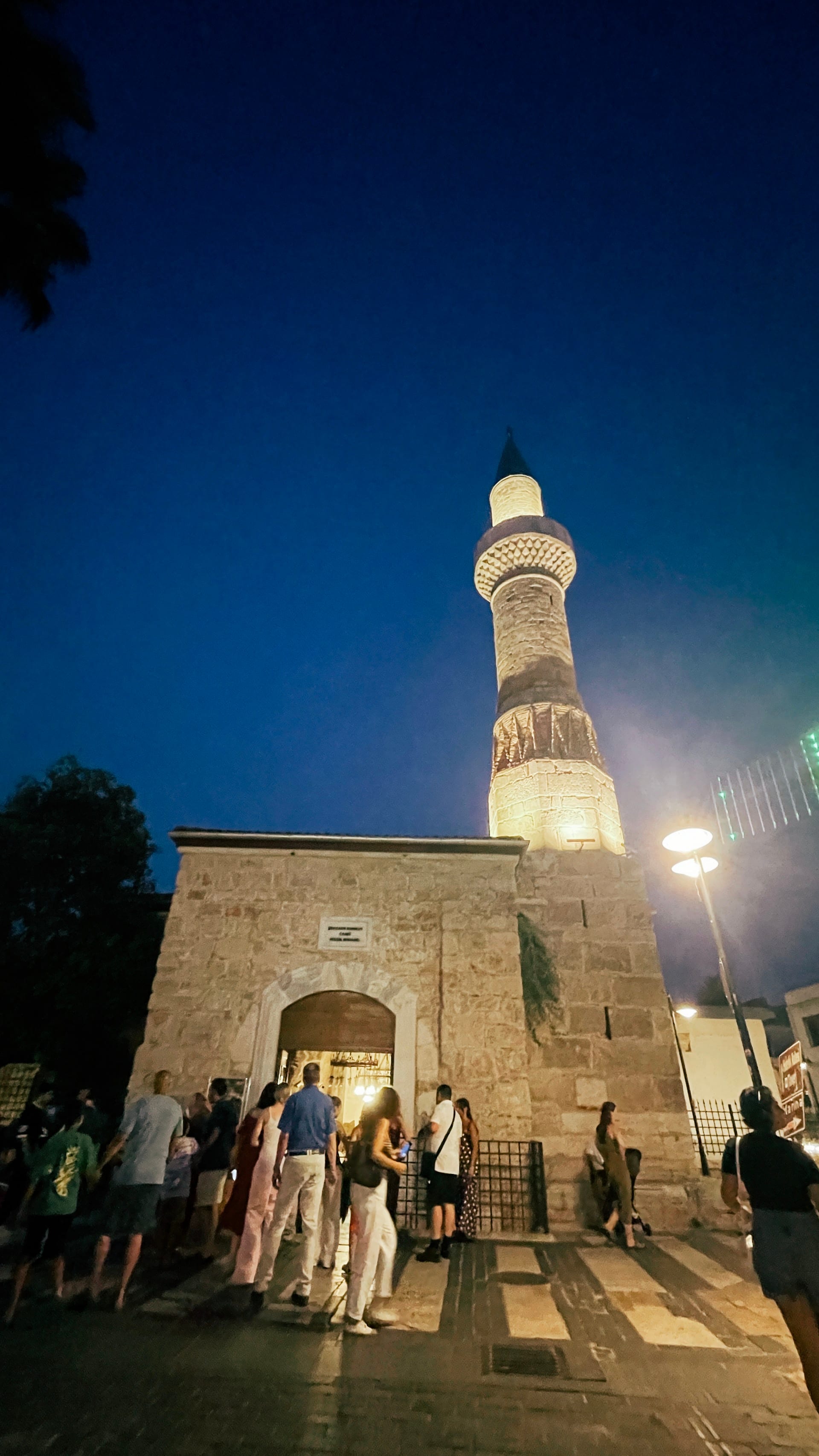 Illuminated minaret and mosque entrance under a deep blue night sky.