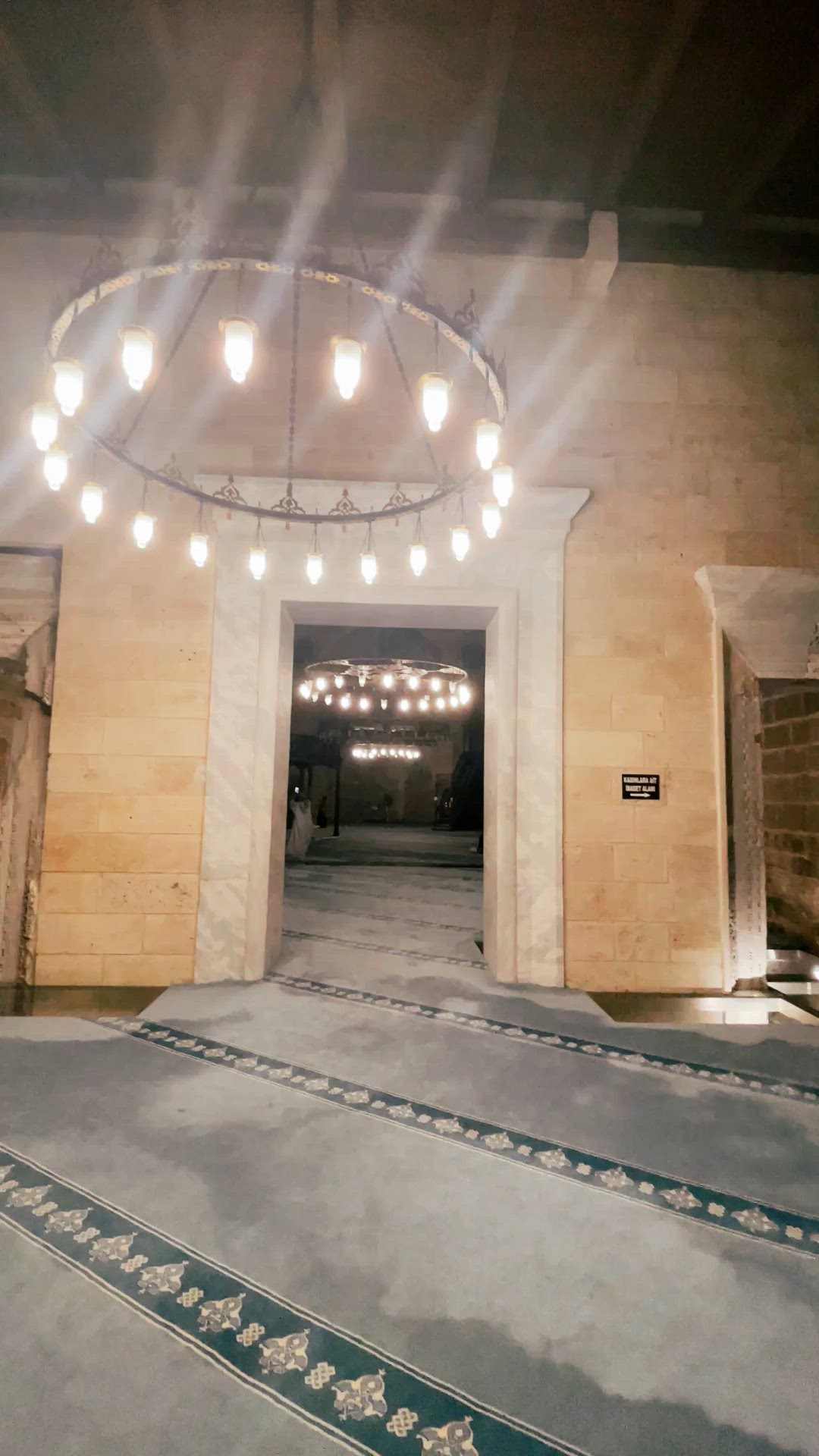 Slow video pan across an open stone prayer hall with arches and circular chandeliers.