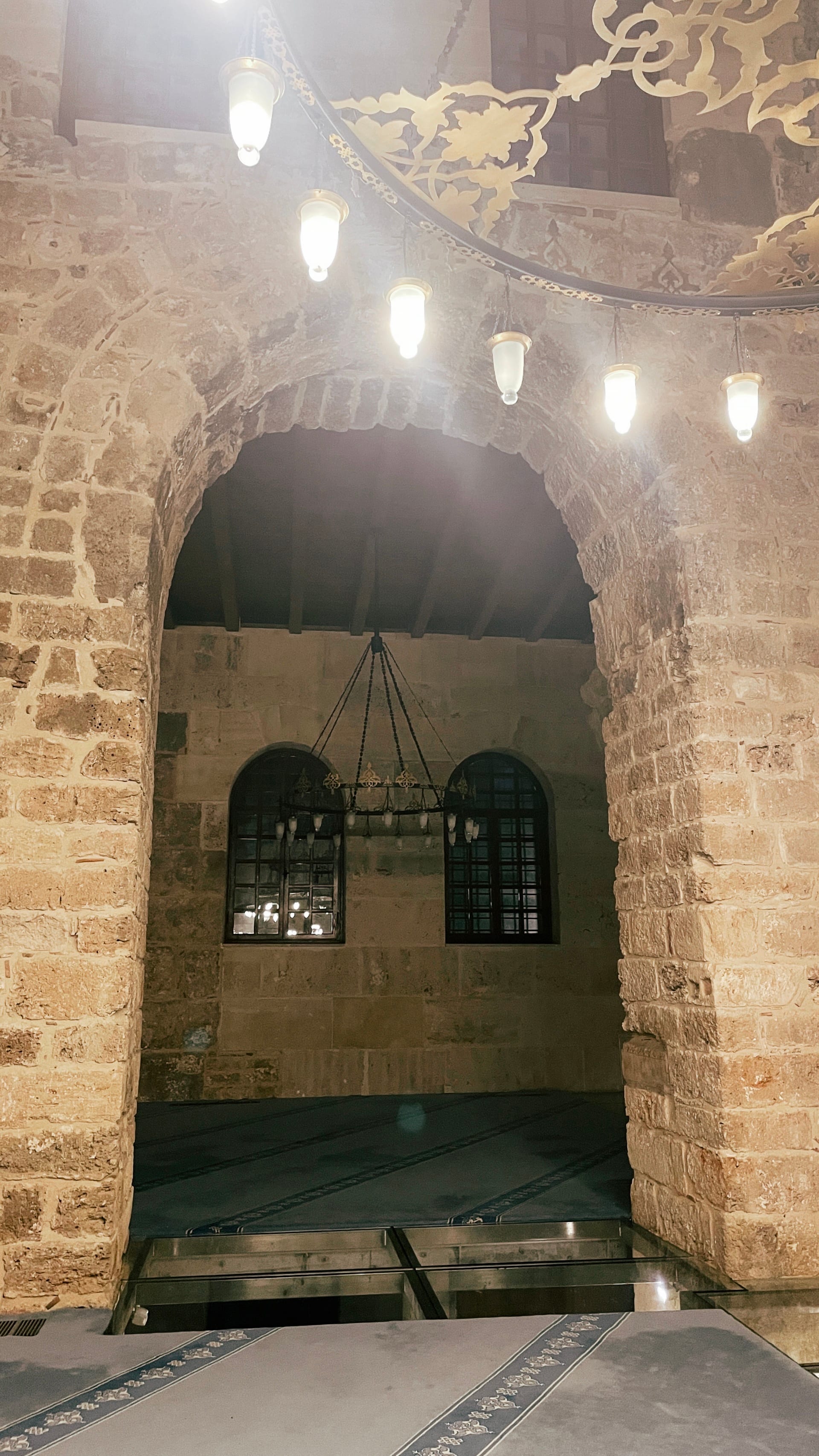 Stone arch above illuminated glass flooring and a room beyond.
