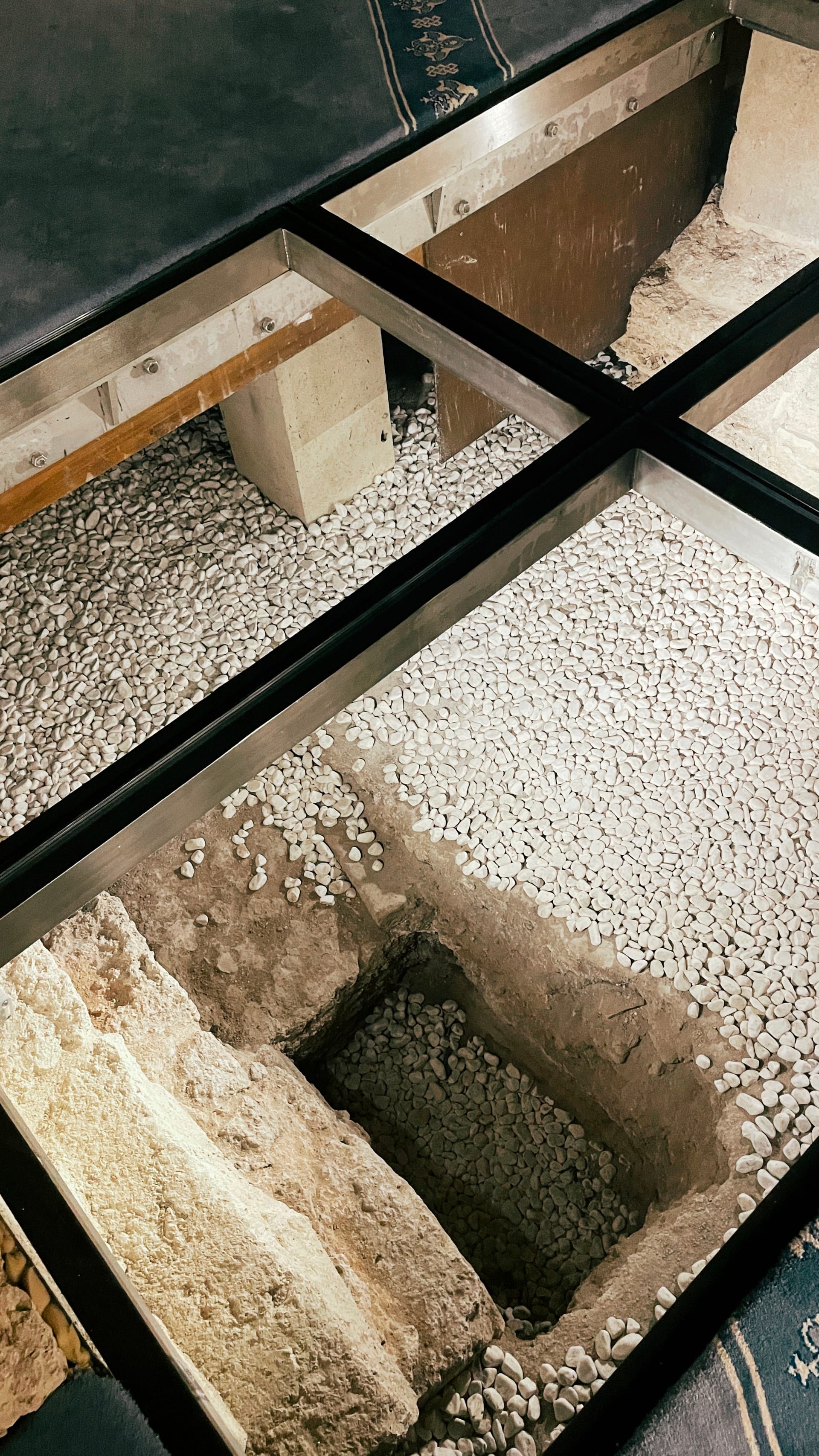 Pale carved stone fragment visible beneath a black-framed glass floor.