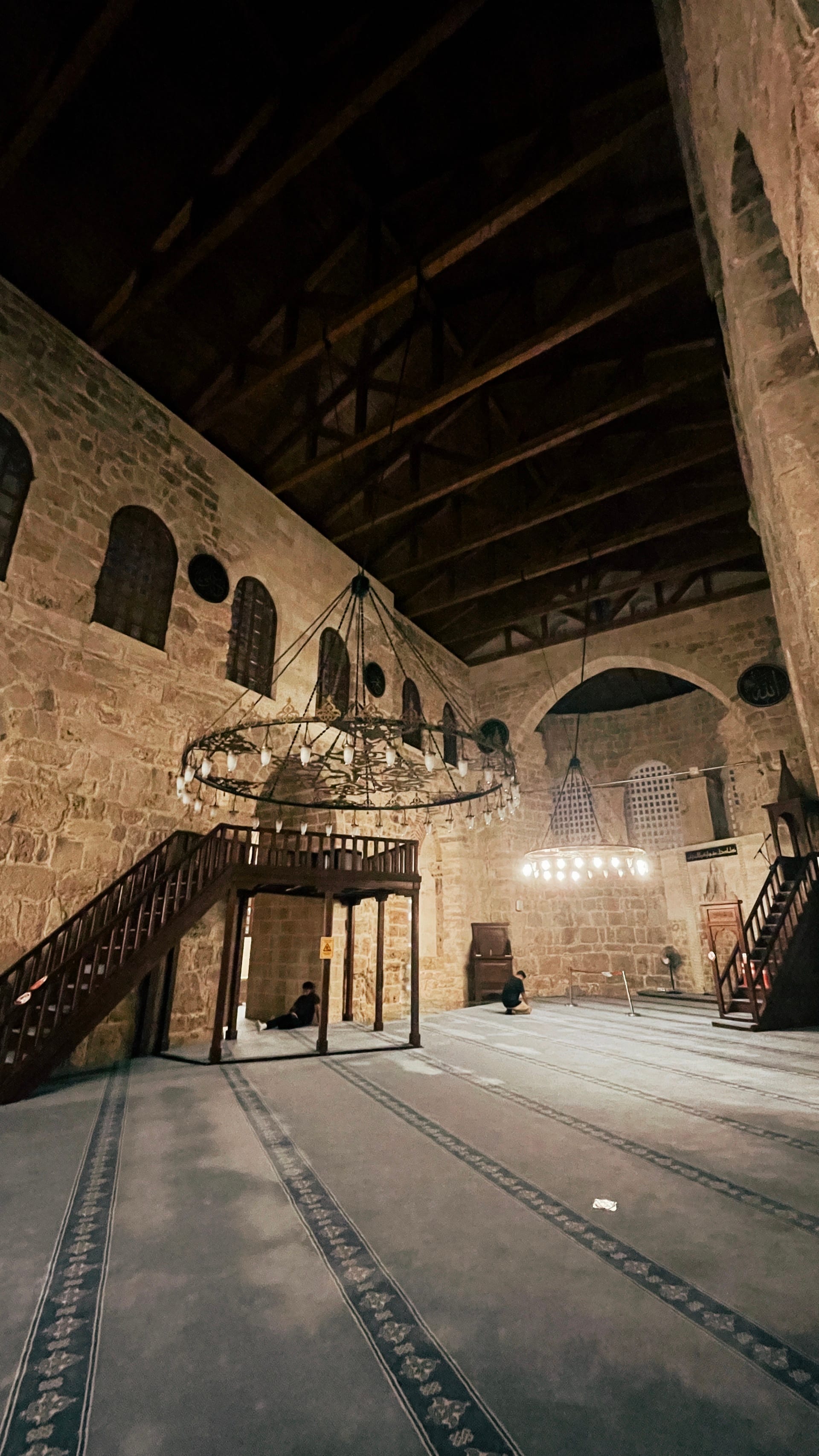 Wide stone prayer hall with chandeliers, timber roof and glass flooring.