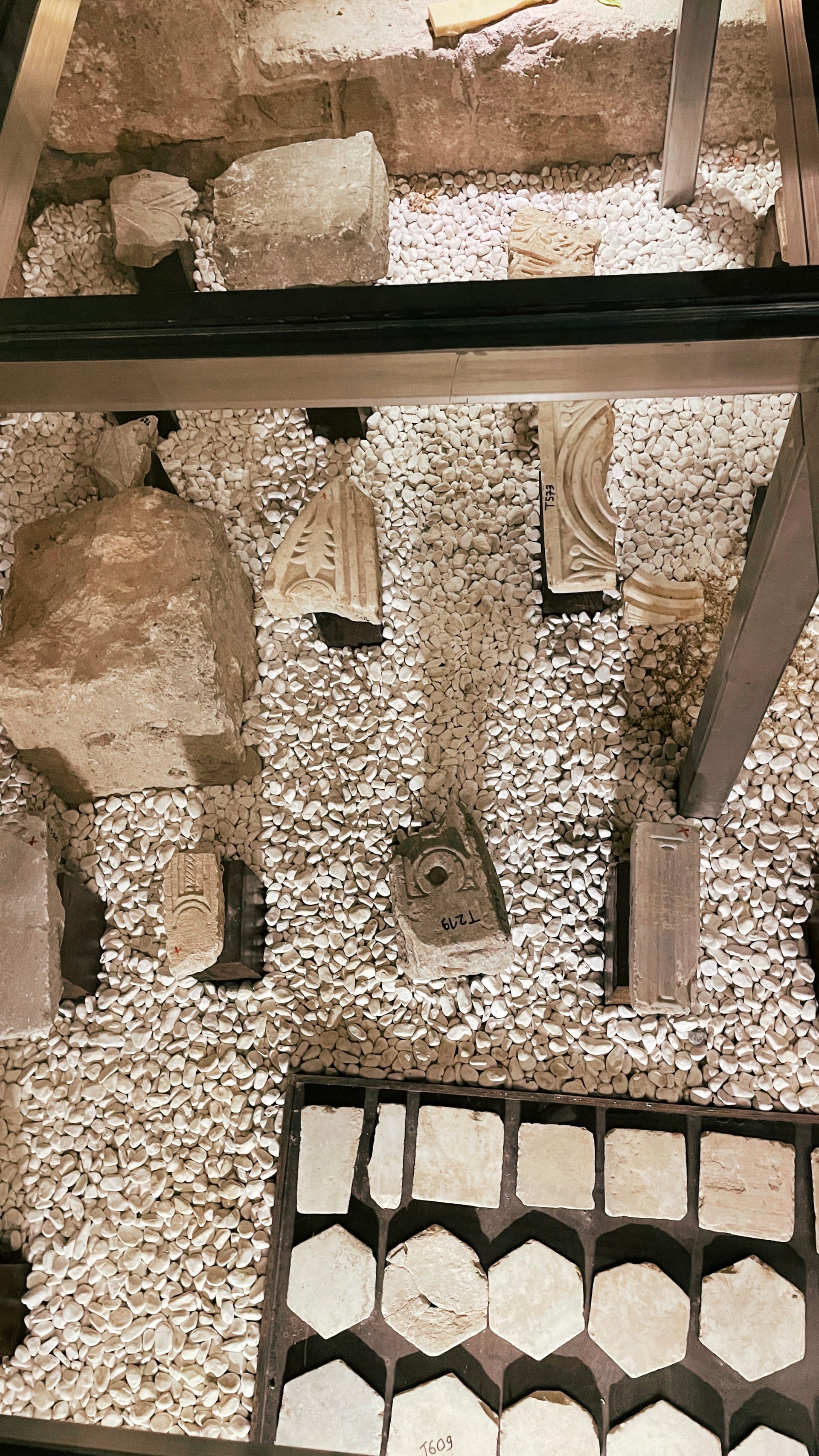 Mixed carved fragments and a geometric group of pale tiles beneath glass.