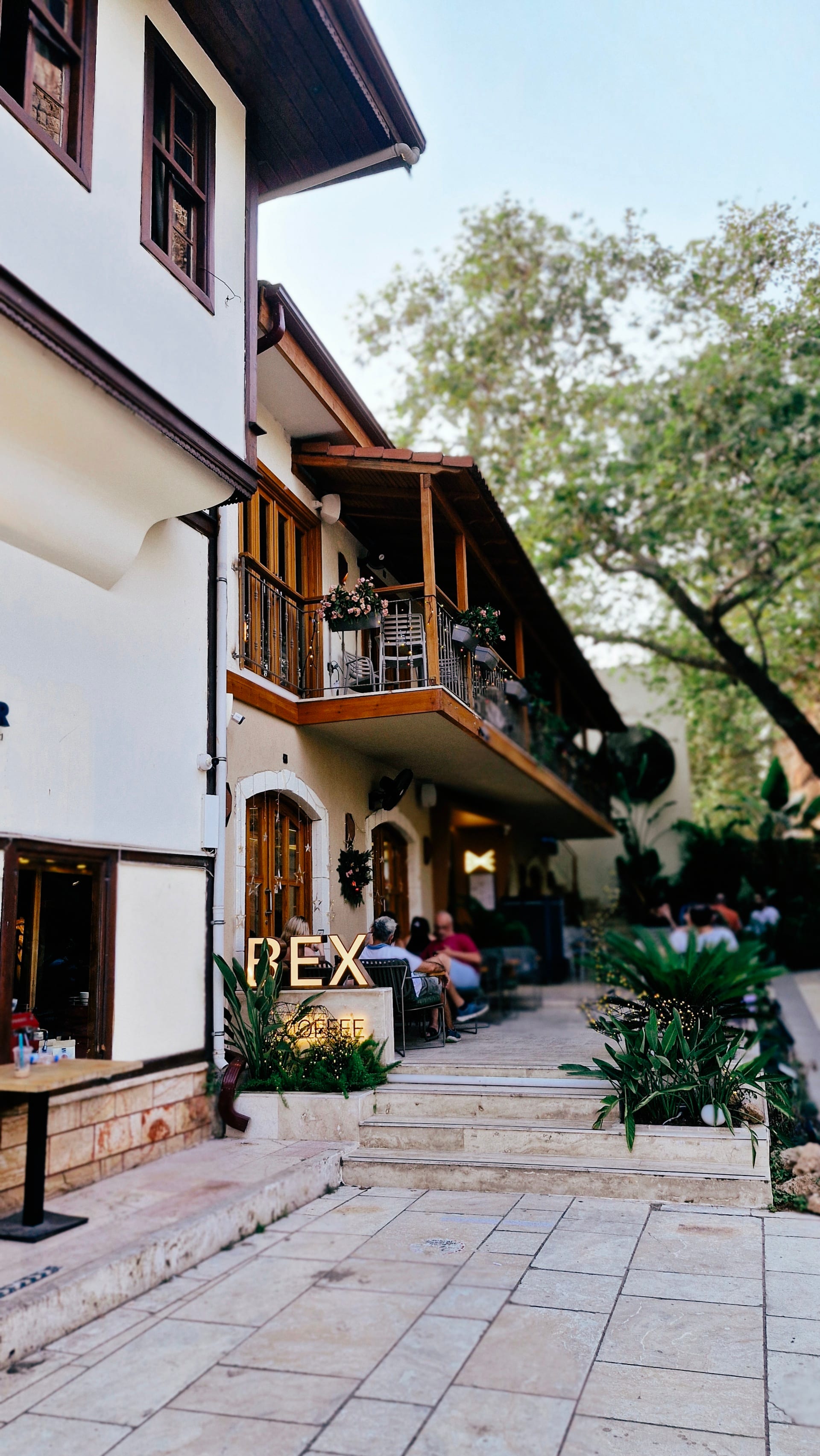White timbered houses and a leafy courtyard beside a stone-paved lane.