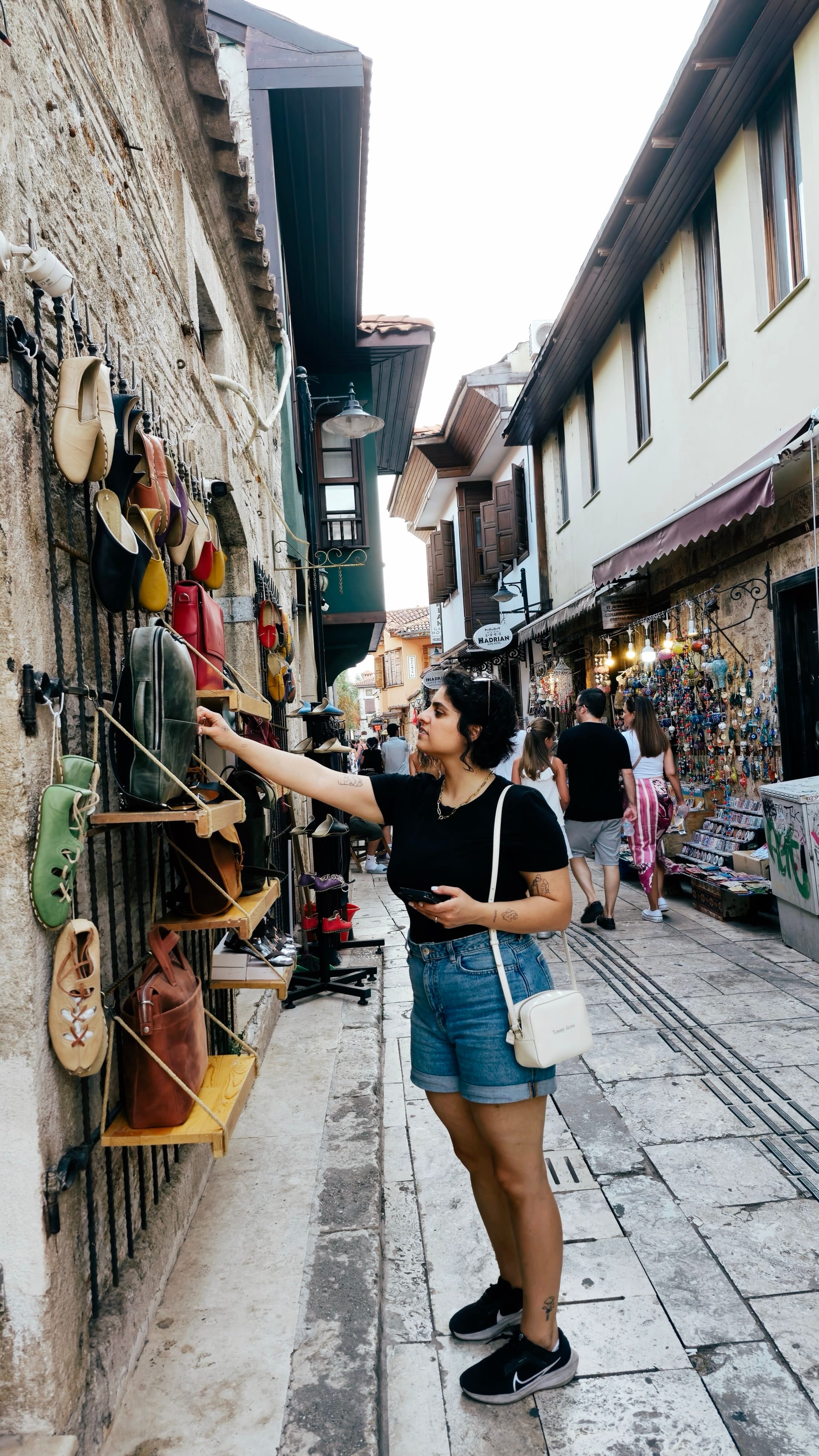 Woman examining handmade shoes displayed on an old stone shopfront.