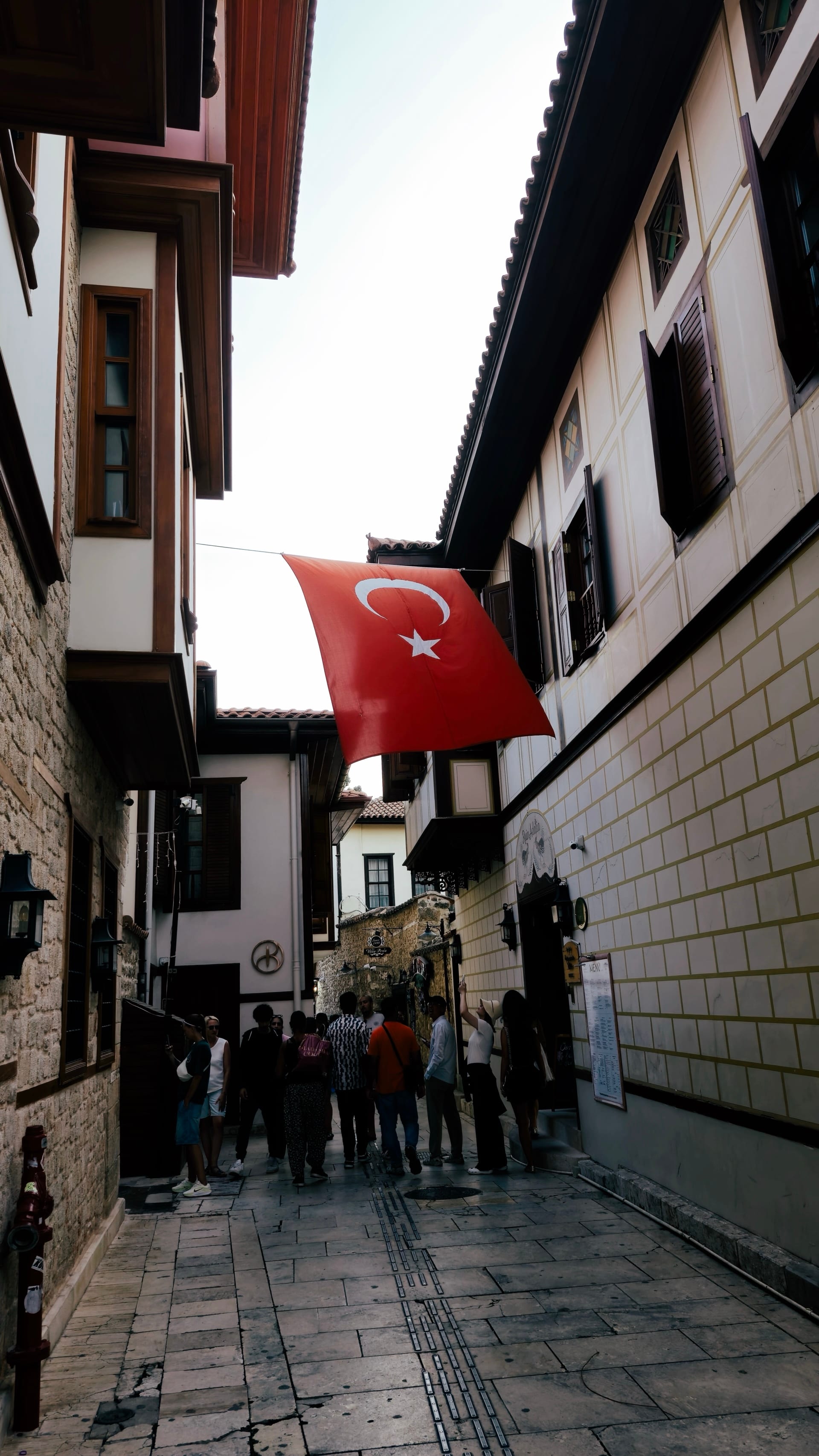 A large Turkish flag hangs between white timbered houses above pedestrians.