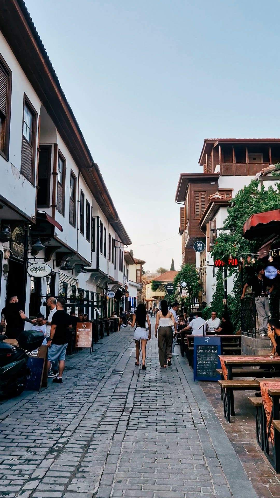 Diners and pedestrians gather outside a long white timbered building.