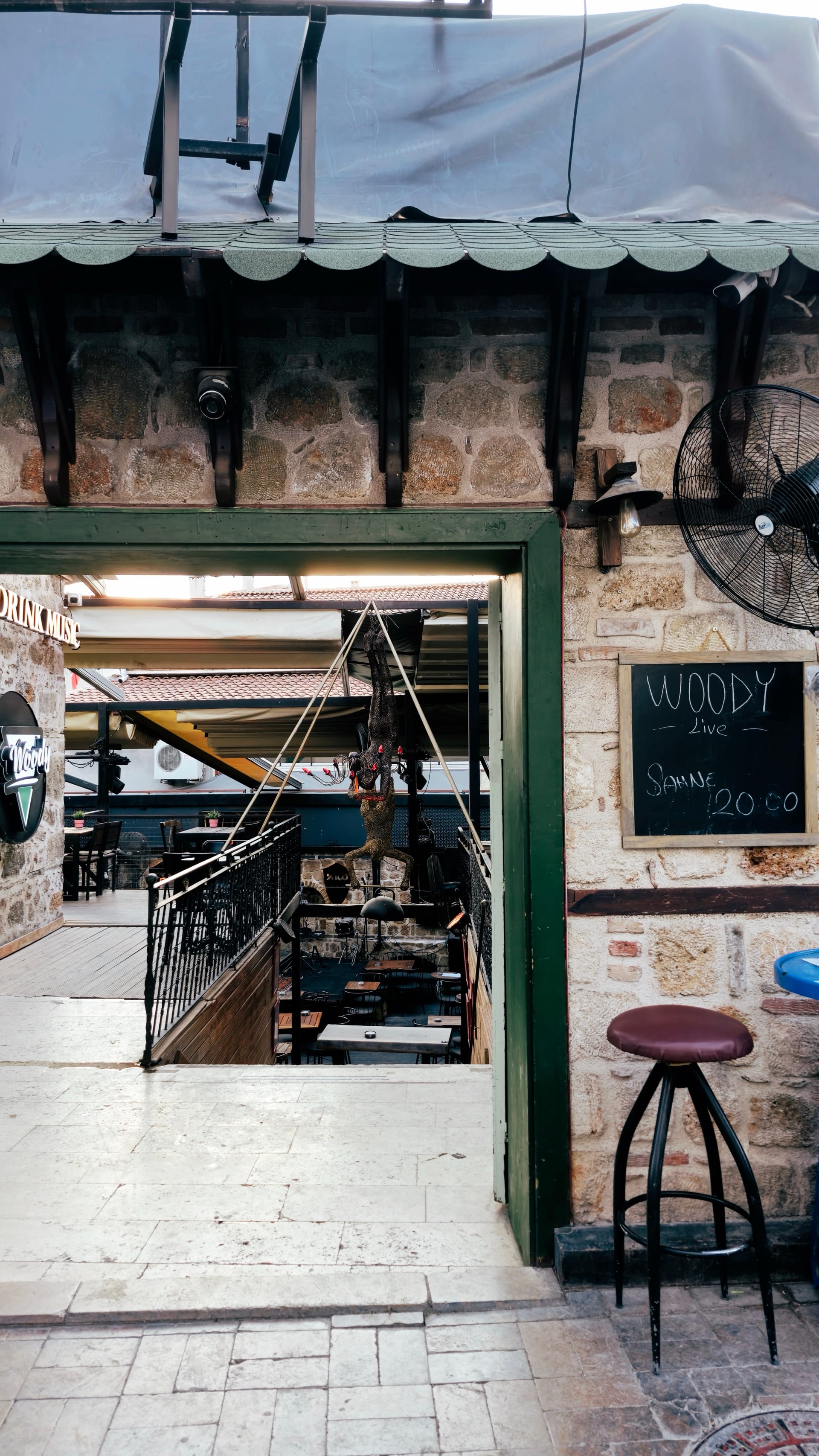An open service window in a stone wall has a stool and chalkboard beside it.