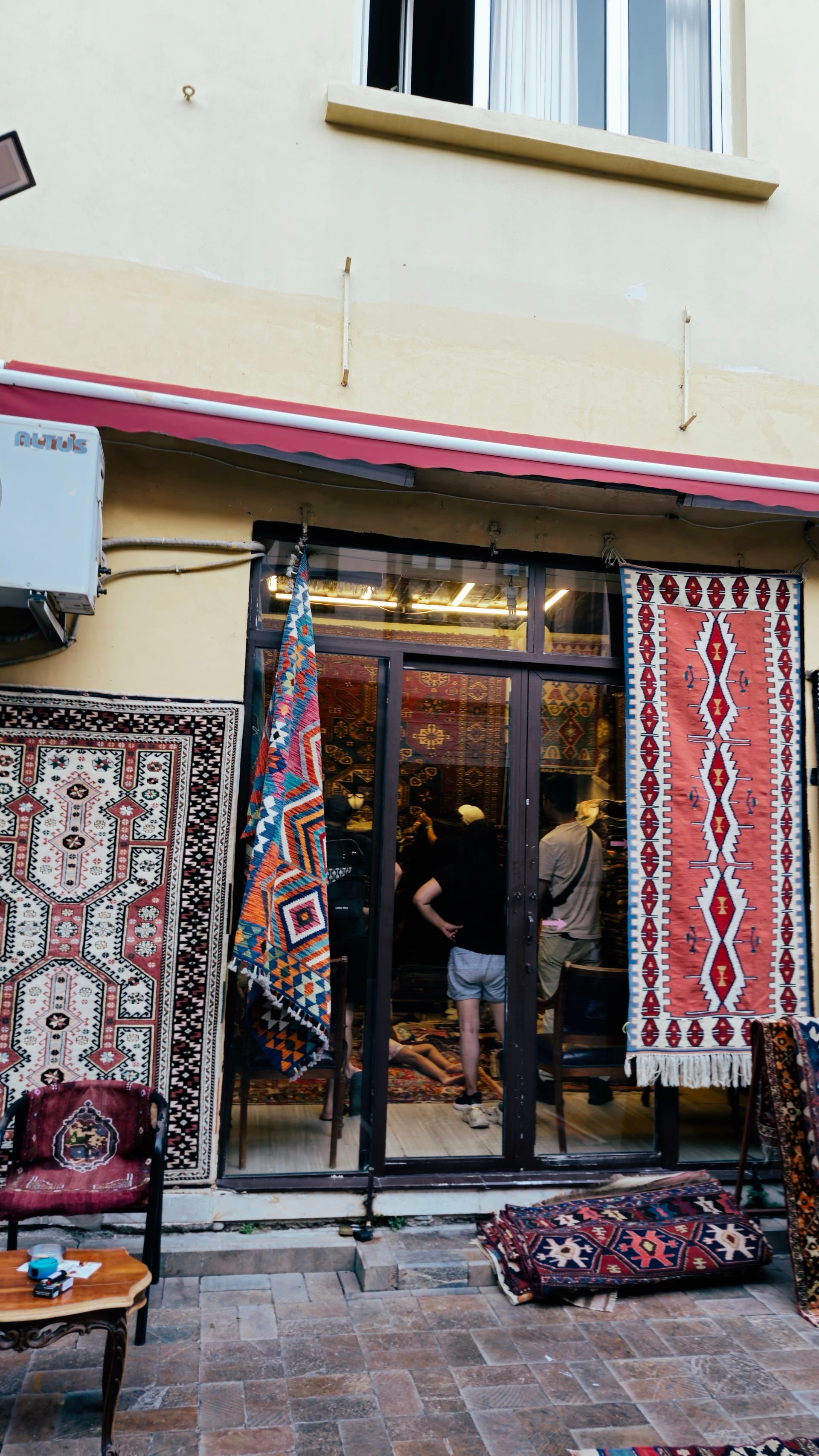 Patterned rugs hang around the entrance of a small textile shop.