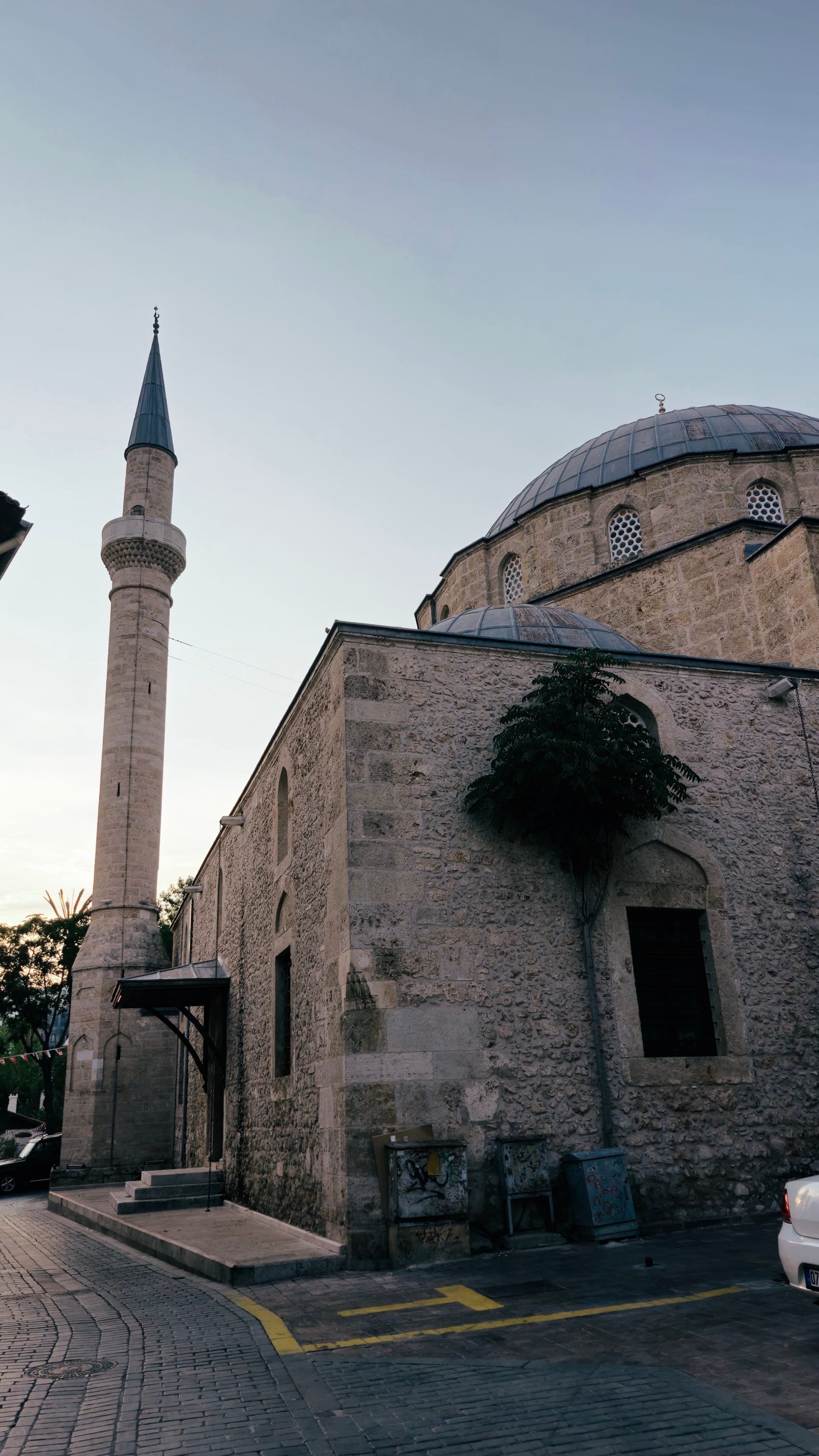 A domed stone mosque and slender minaret stand beside a paved lane.