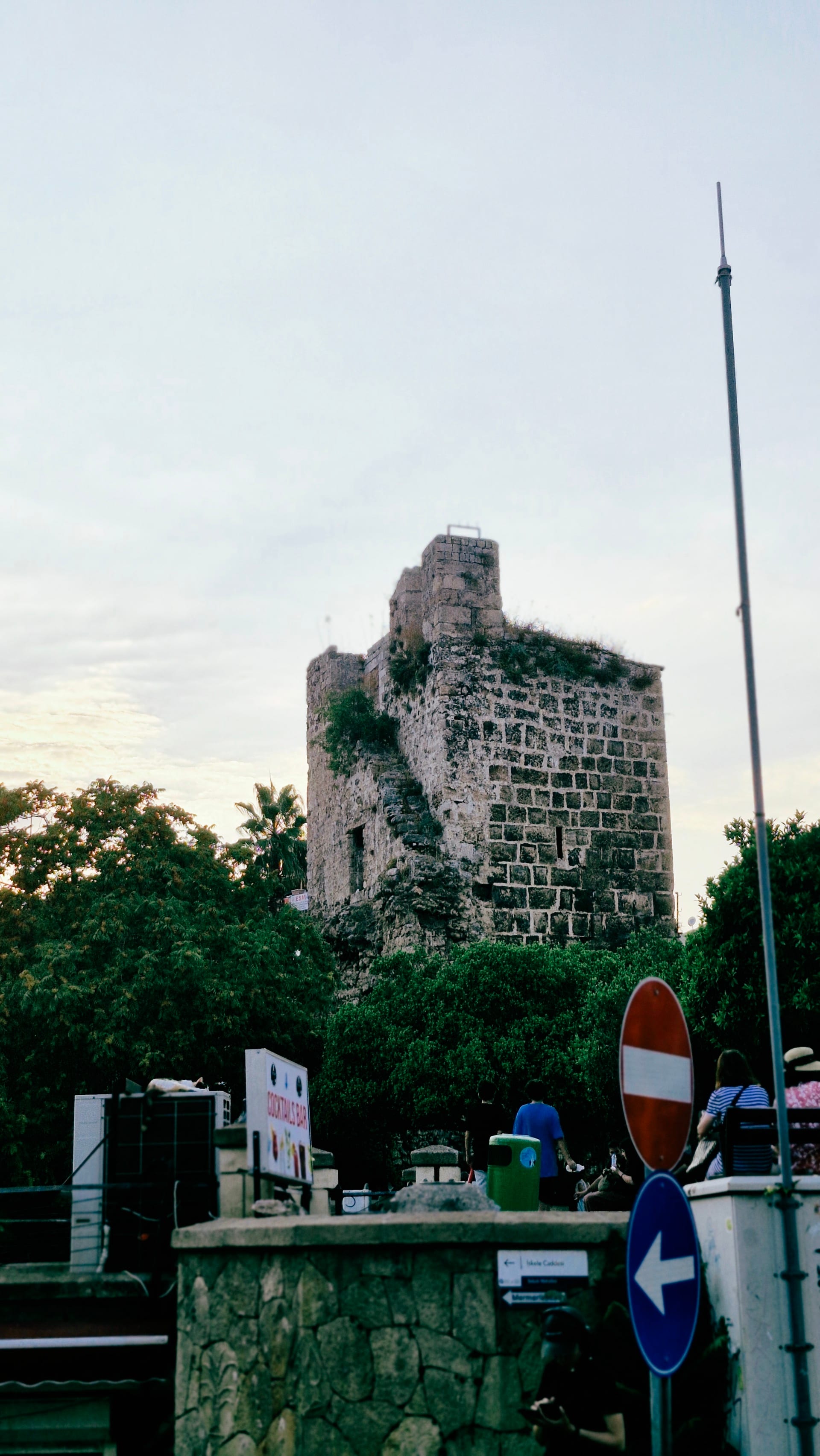 A ruined stone tower rises behind trees and roadside direction signs.