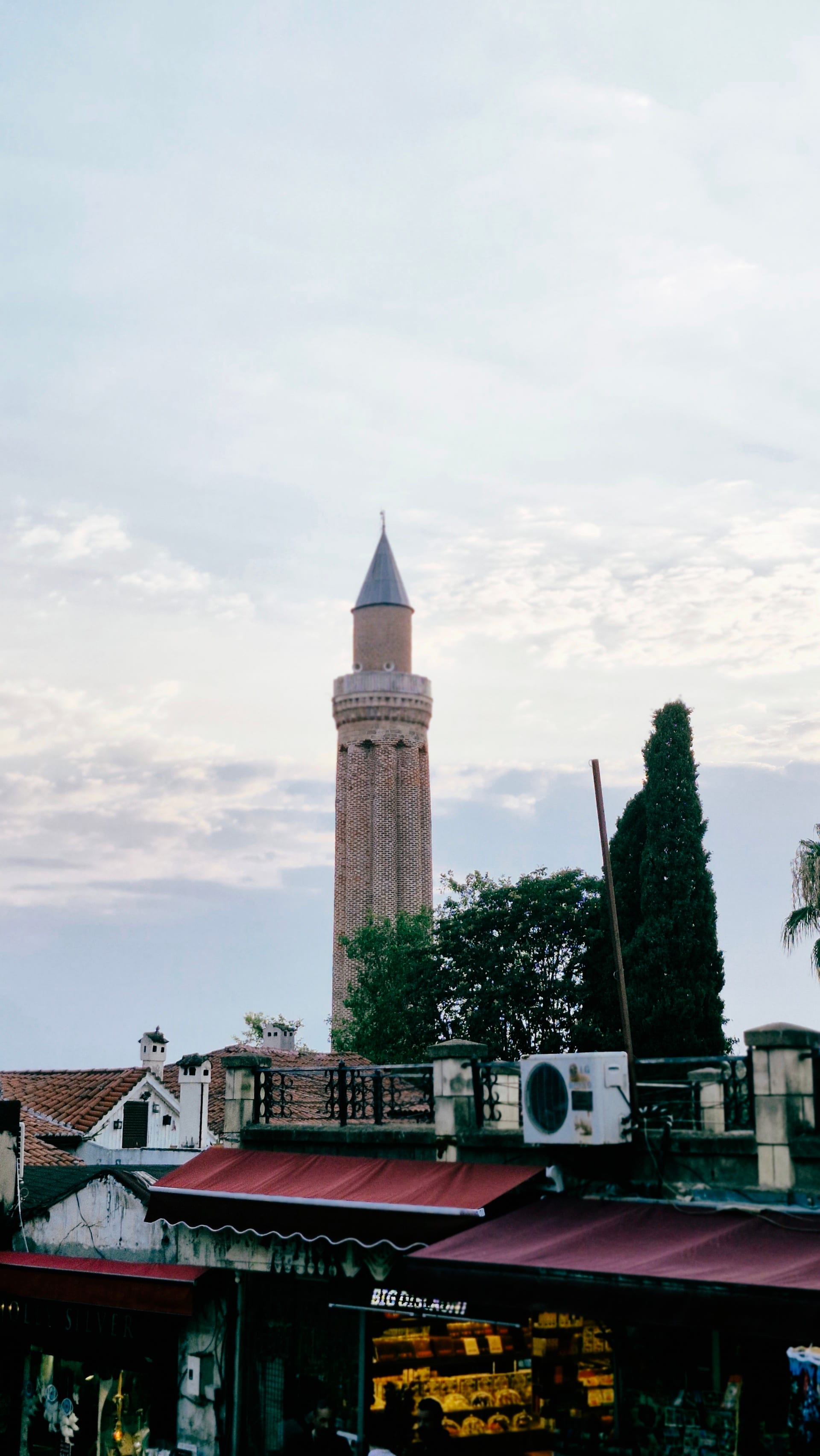 A slender brick minaret rises above tiled roofs and a red awning.