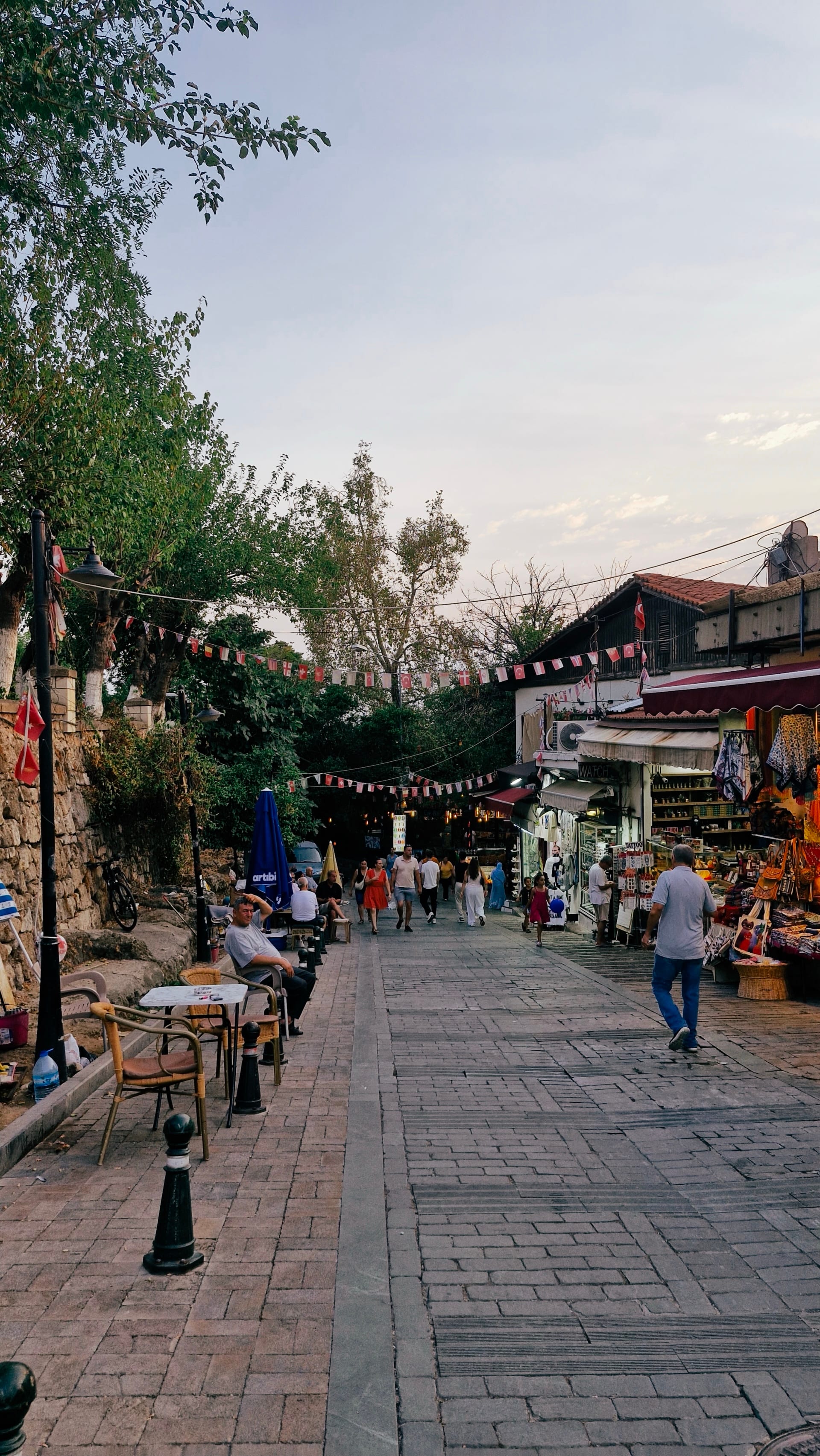 Twilight pedestrian lane lined with café tables, shops and strings of flags.