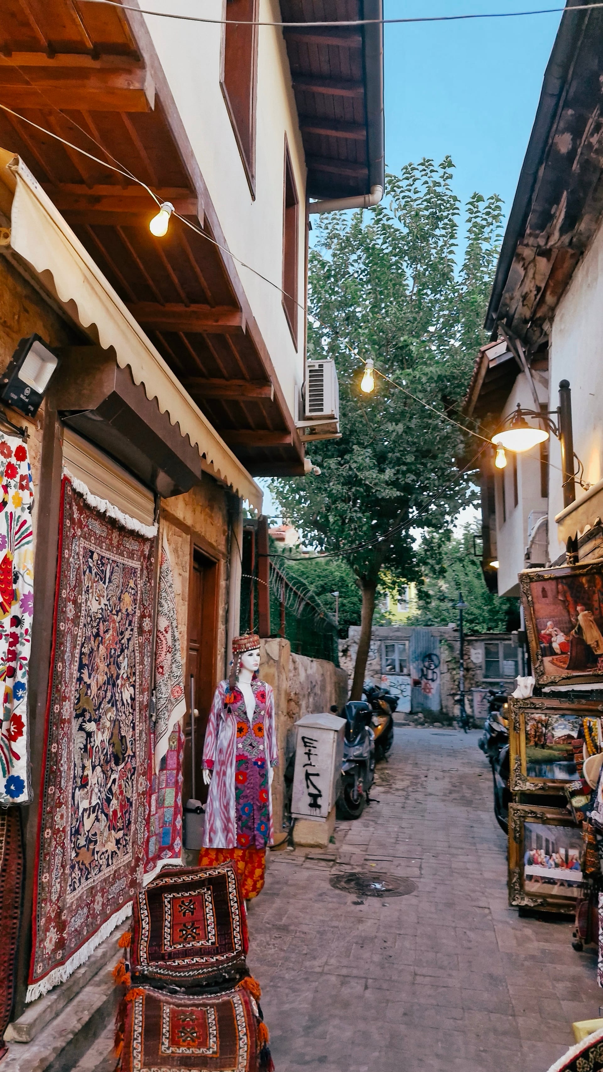Patterned carpets hang outside shops along a narrow evening lane.