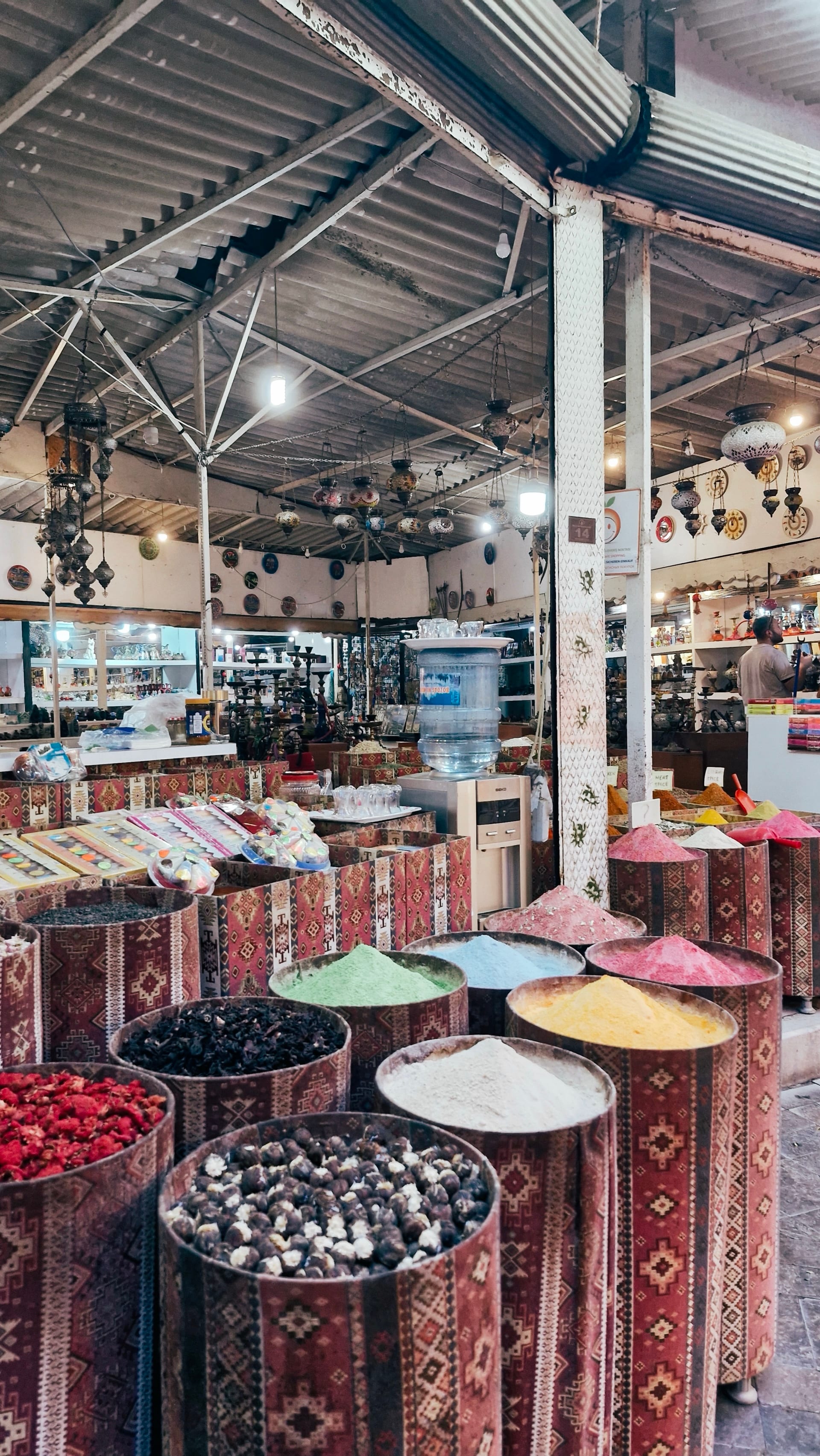 Open bins of colorful spices and dried goods fill a covered market stall.