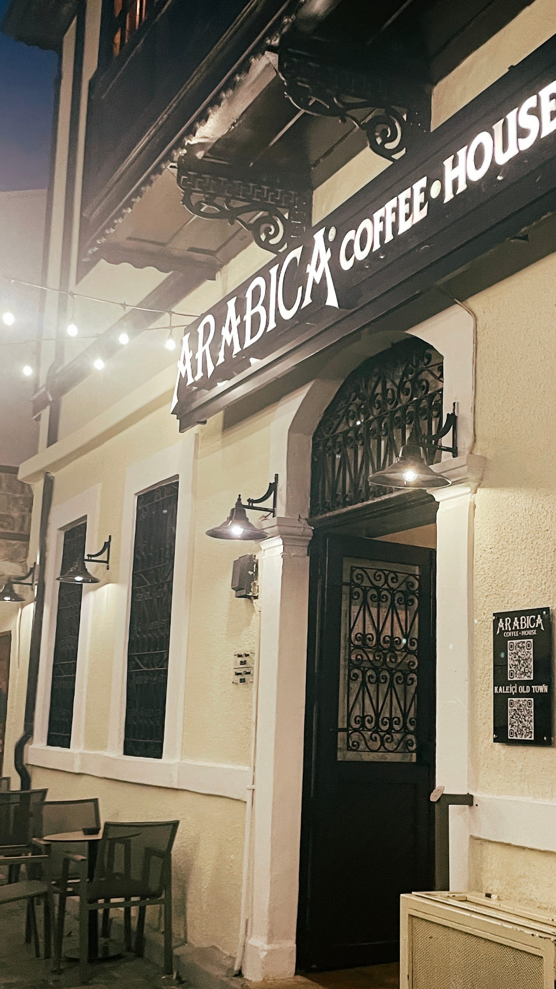 The illuminated façade of a coffeehouse faces a narrow street at night.